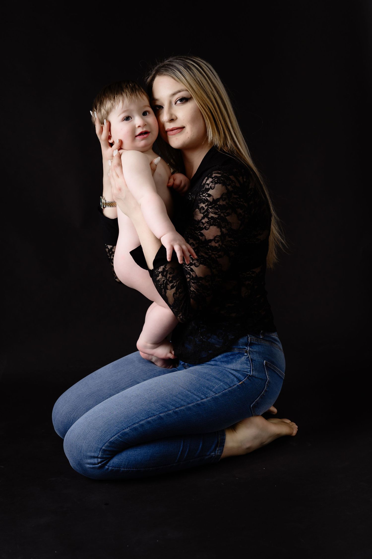 Studio portrait against dark background showing tender moment between parent and child.