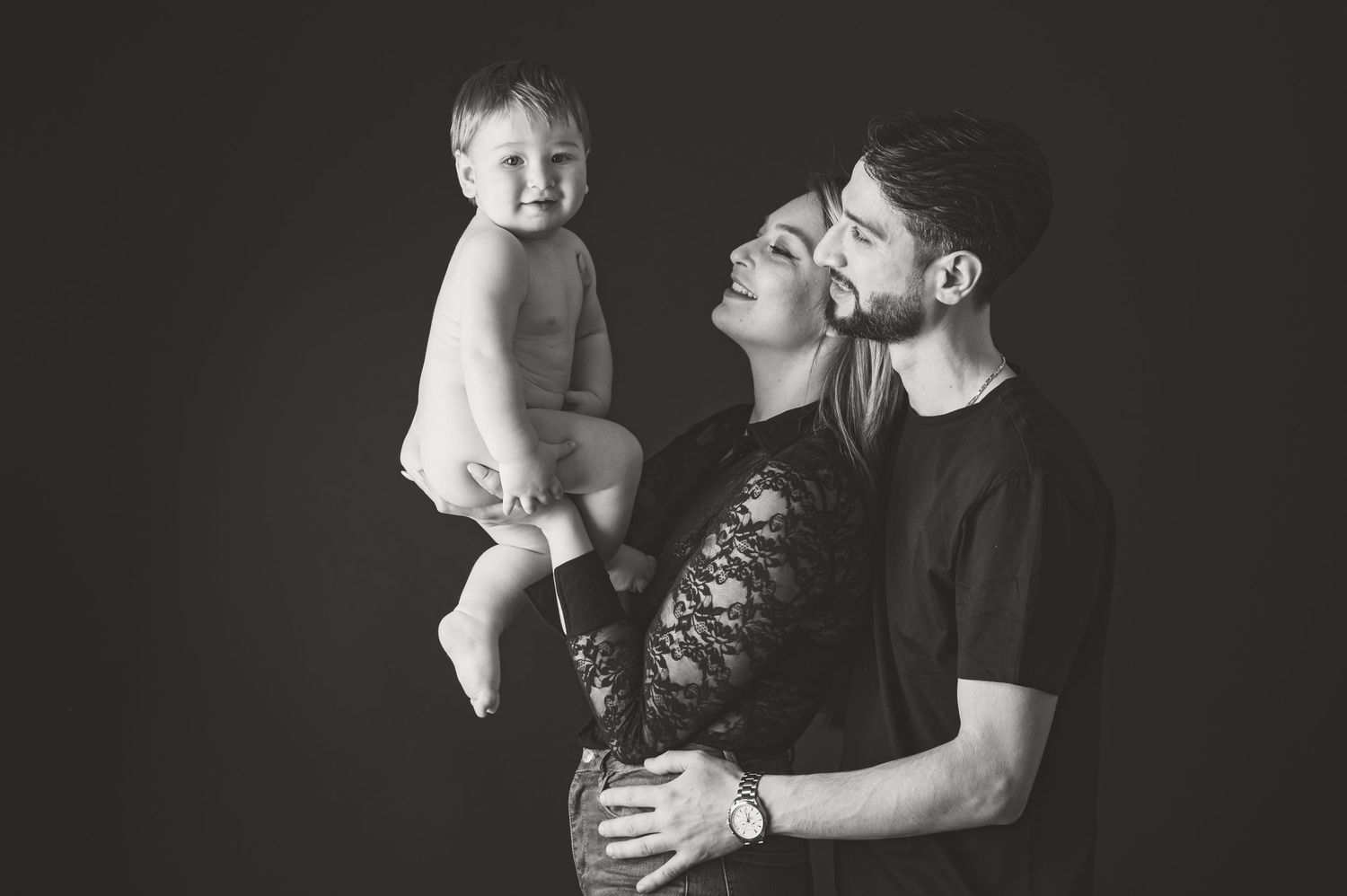 Black and white family portrait showing intimate moment against dark background.