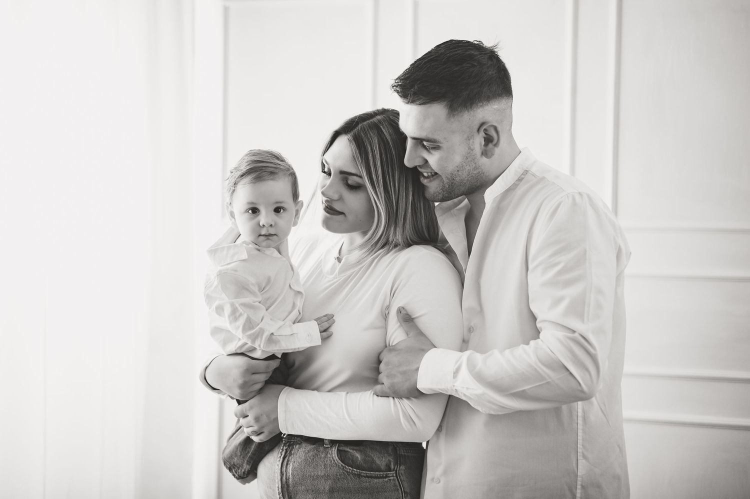 Family portrait in white room showing intimate moment between parents and child.