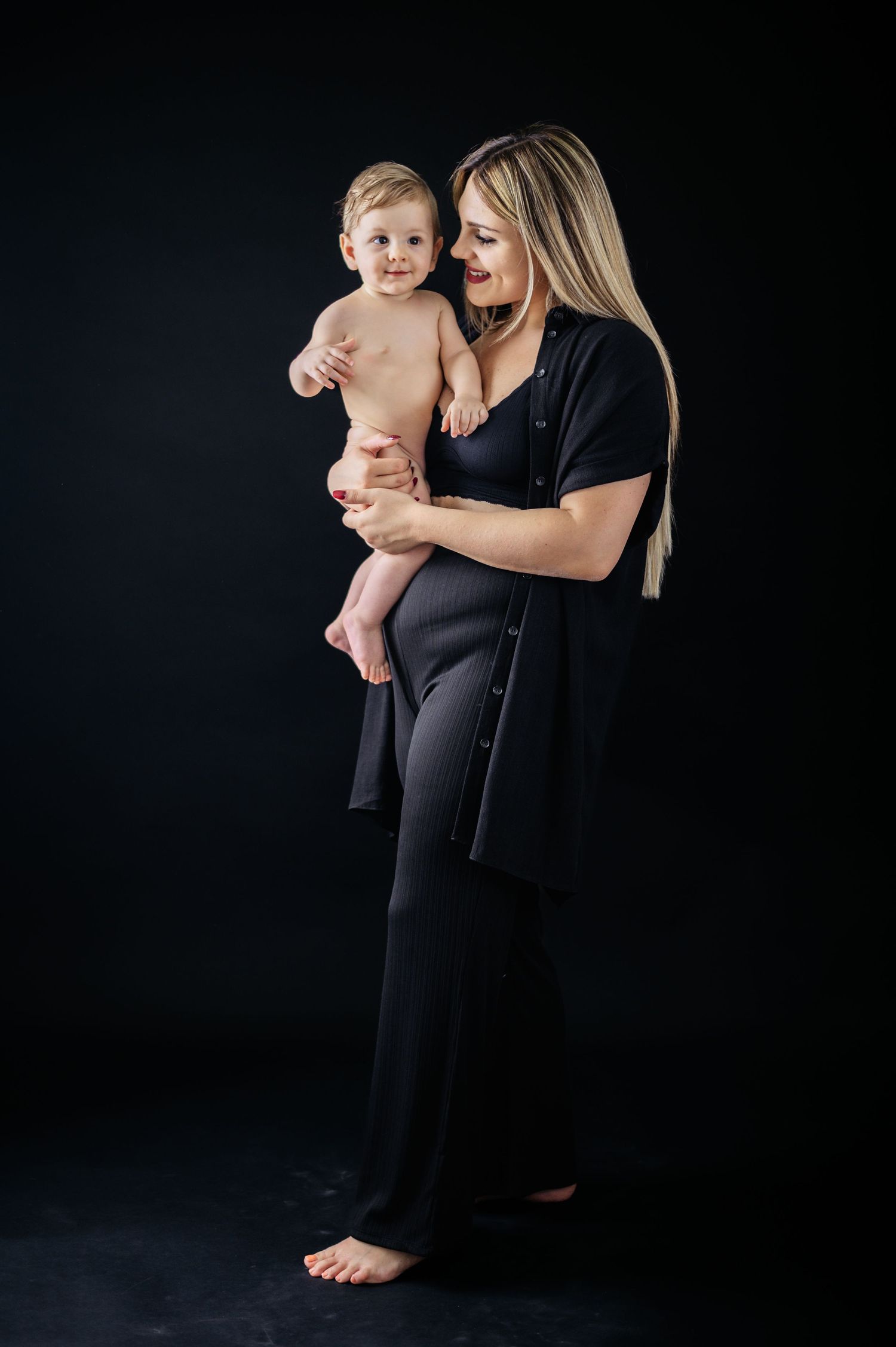 Studio portrait against black background showing tender moment between parent and baby.