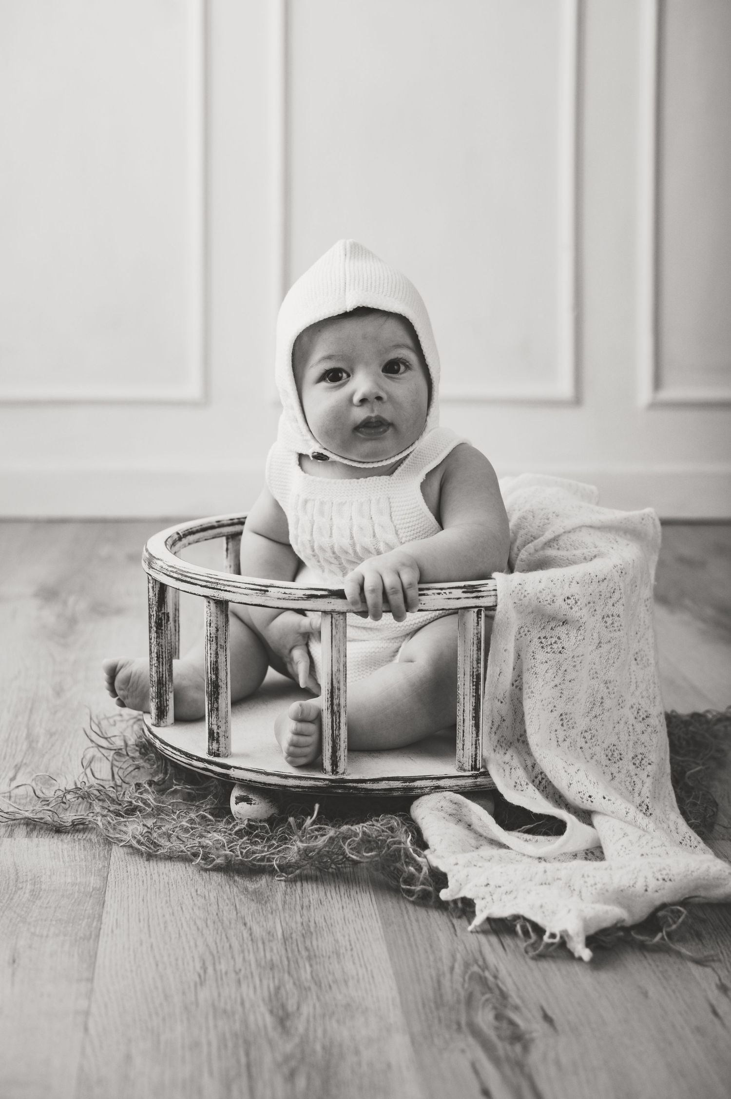Black and white photo of an infant sitting in a vintage wooden container on hardwood floor.