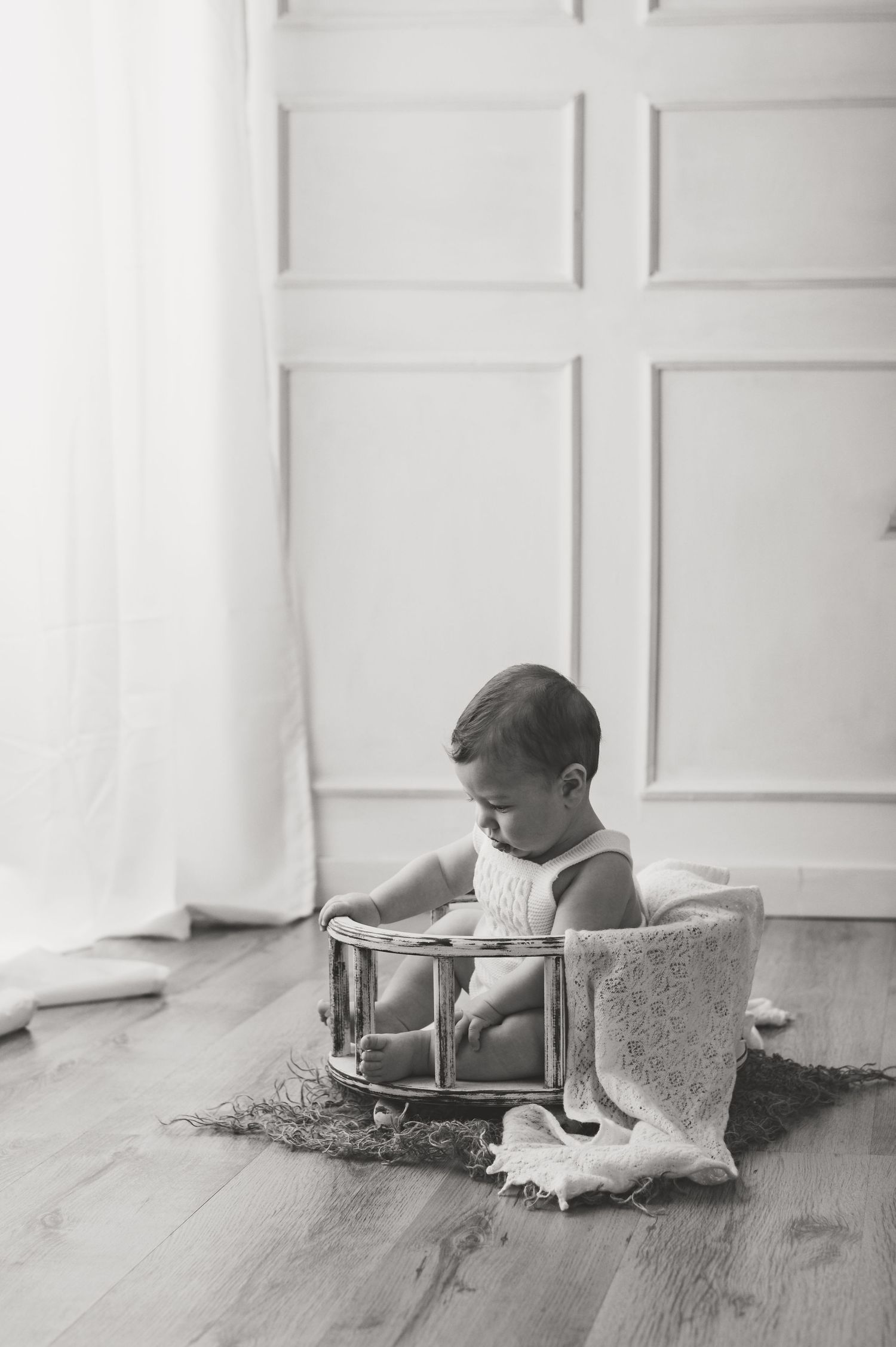 Black and white photo of child sitting in vintage wooden container near white paneled wall.