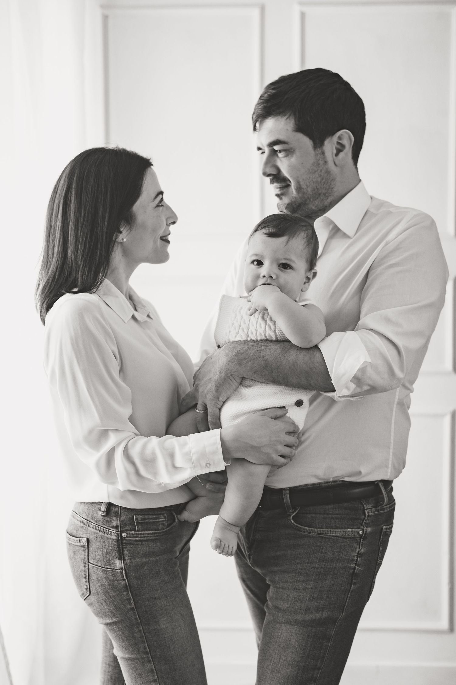 Black and white family portrait showing parents in casual attire holding their smiling baby.