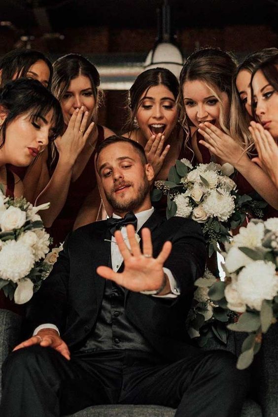 A wedding party poses for a fun photo with white floral bouquets.