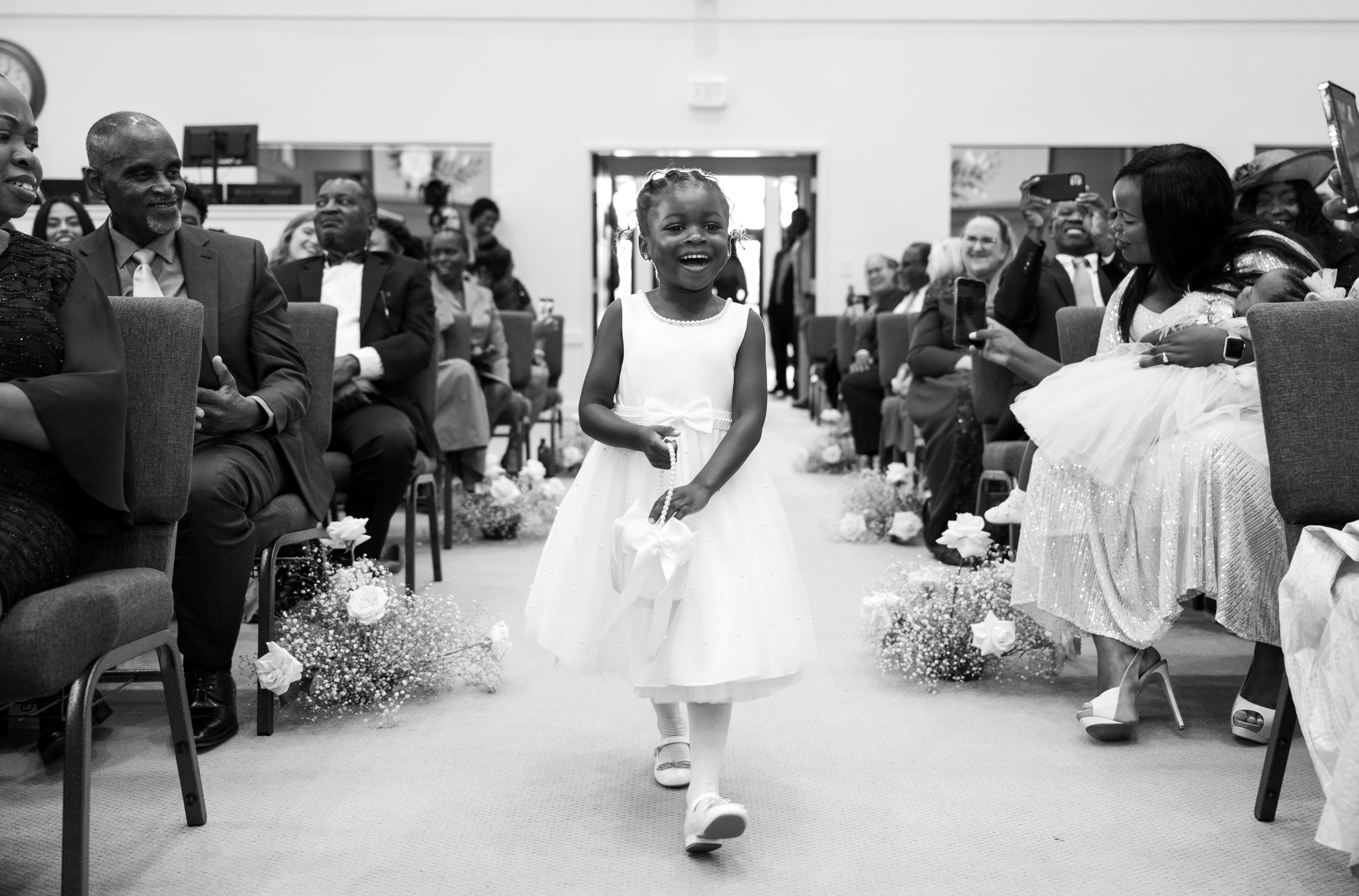 A flower girl in a white dress walks down the aisle during a church ceremony.