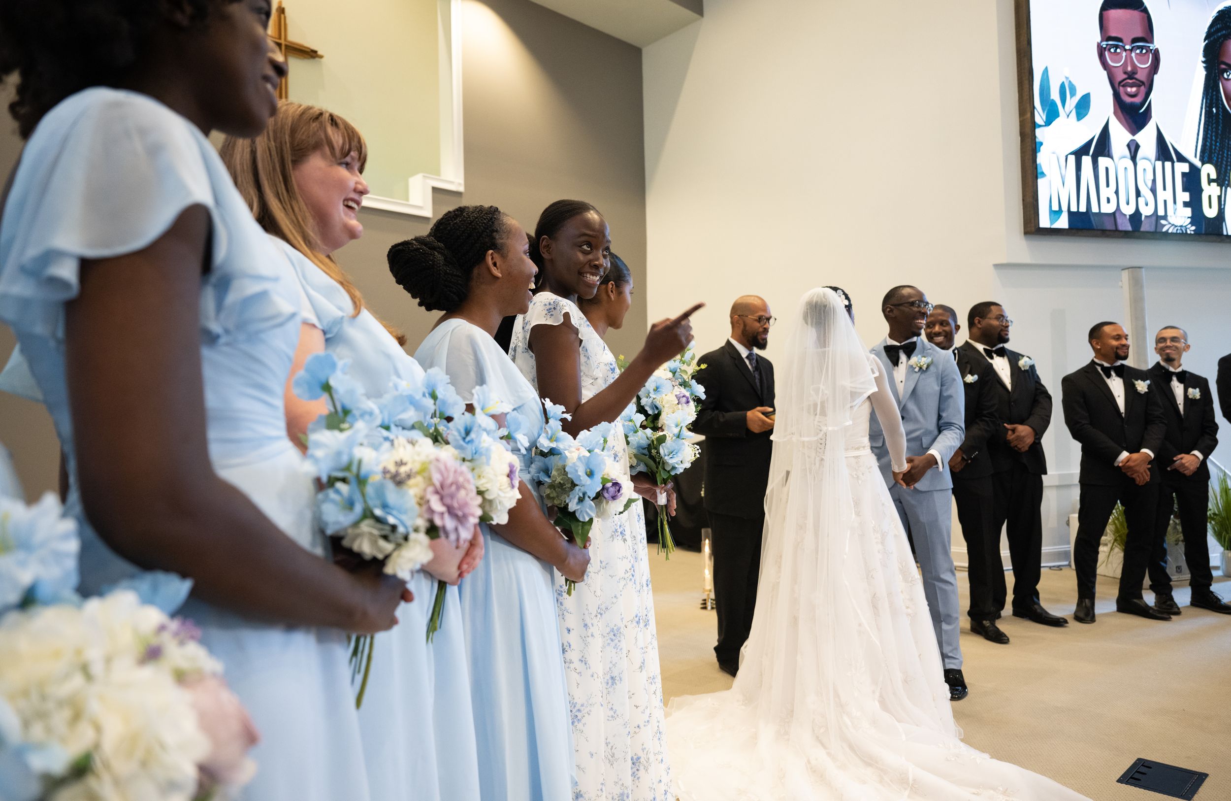 Bridesmaids in powder blue dresses stand beside a wedding dress display.