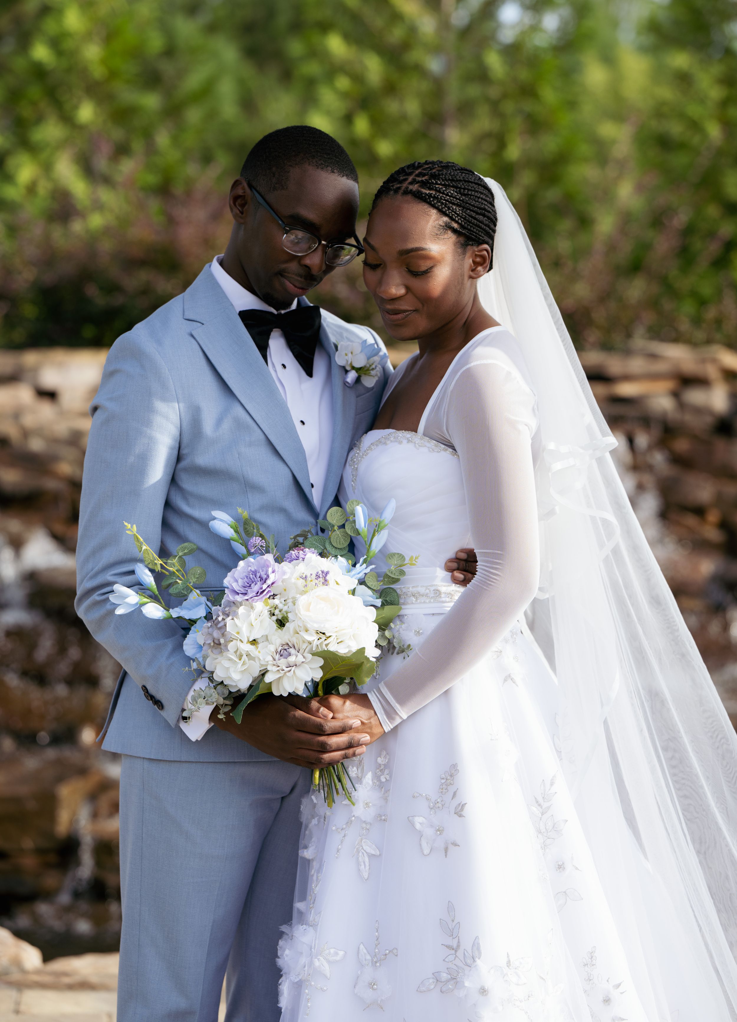 A couple shares an intimate moment in formal wedding attire against a natural backdrop.