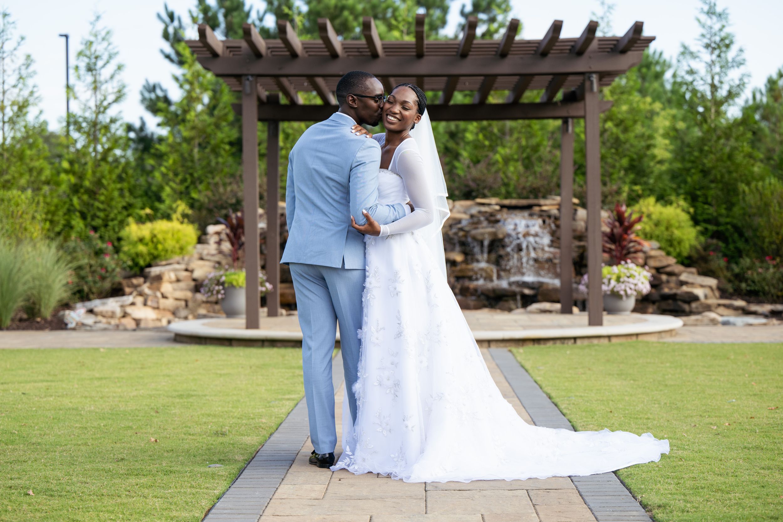 A couple poses for portraits in front of a garden pergola and waterfall.