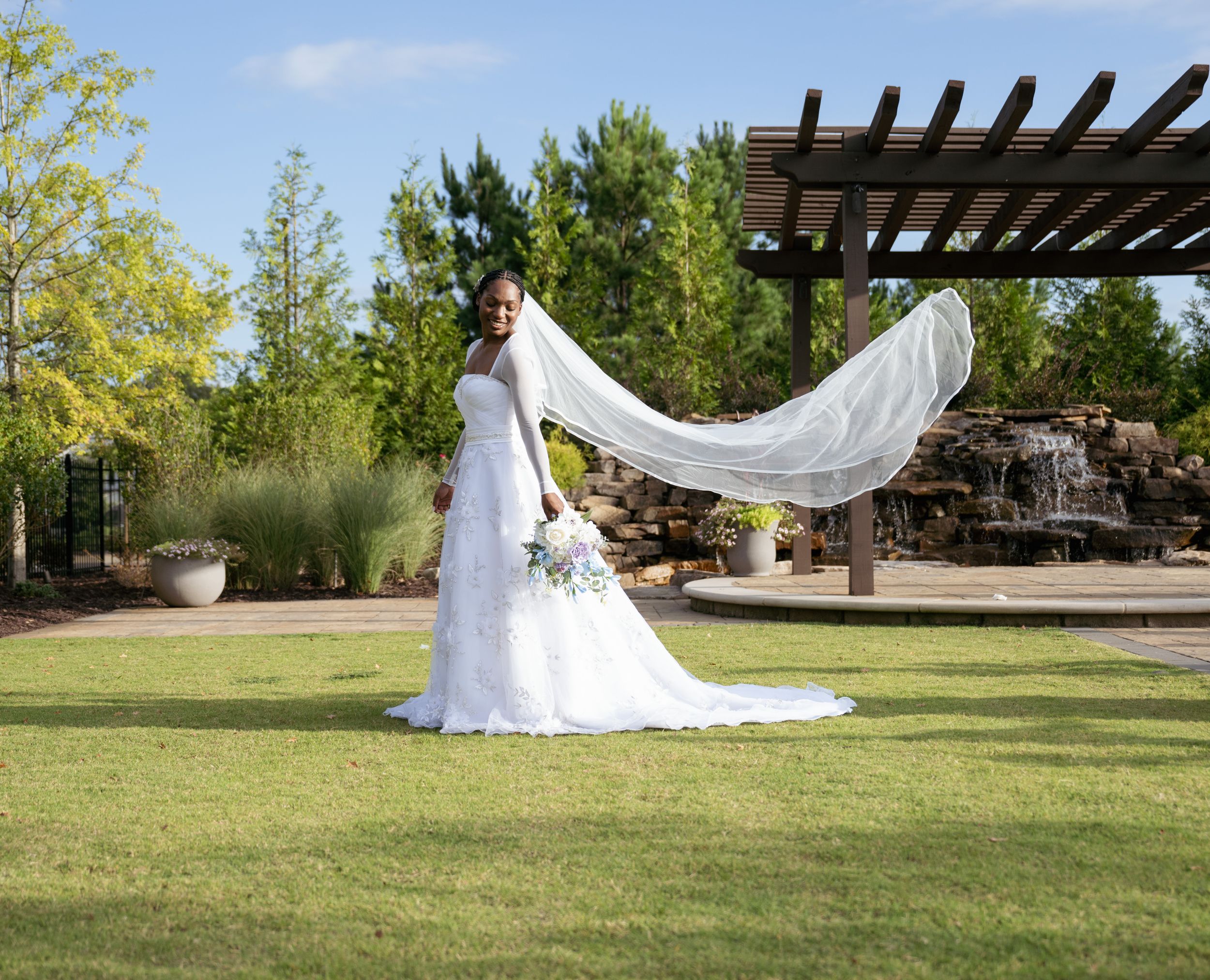 A flowing wedding veil catches the breeze in an outdoor bridal portrait.