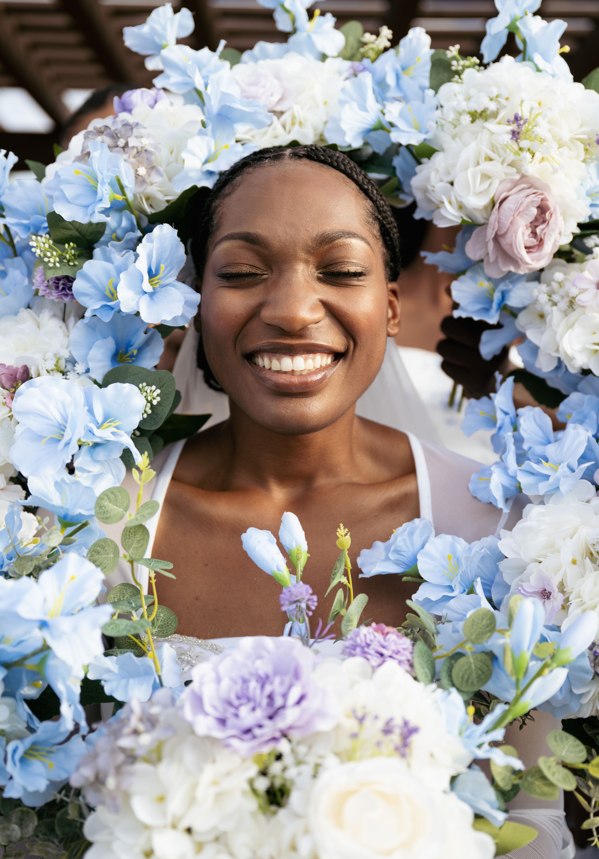 Beautiful floral arrangement of blue and white flowers frames a joyful bridal portrait.