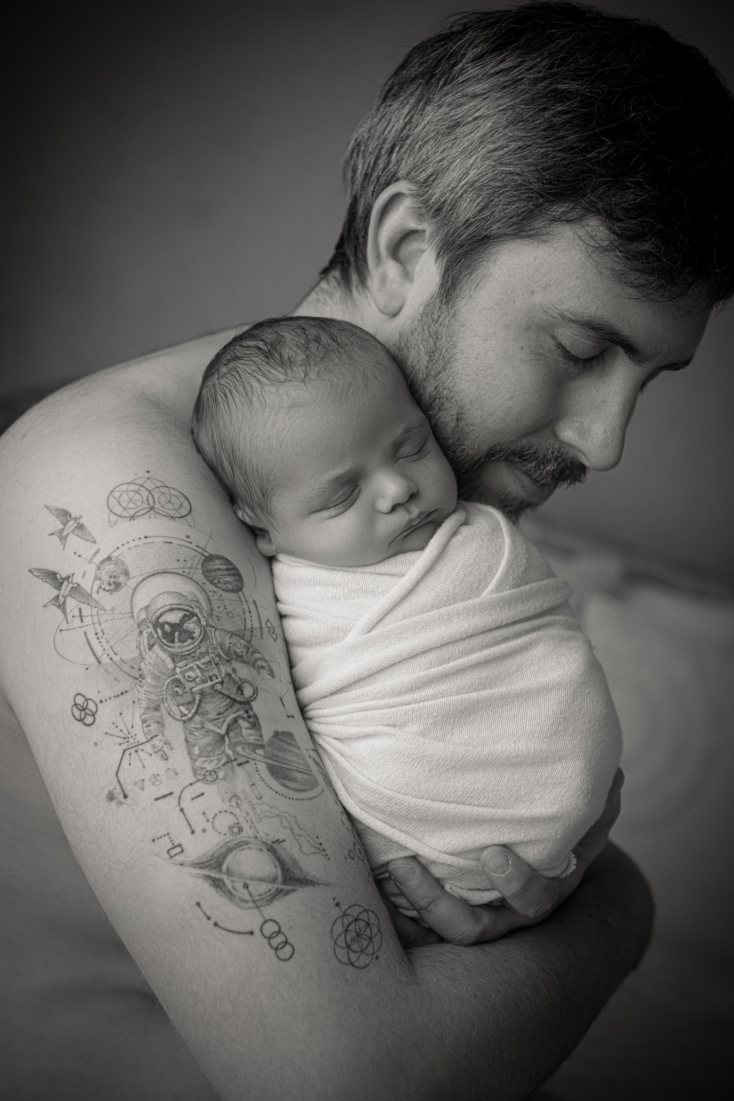 Black and white artistic photo series showing a baby sleeping peacefully against dad's tattooed shoulder.