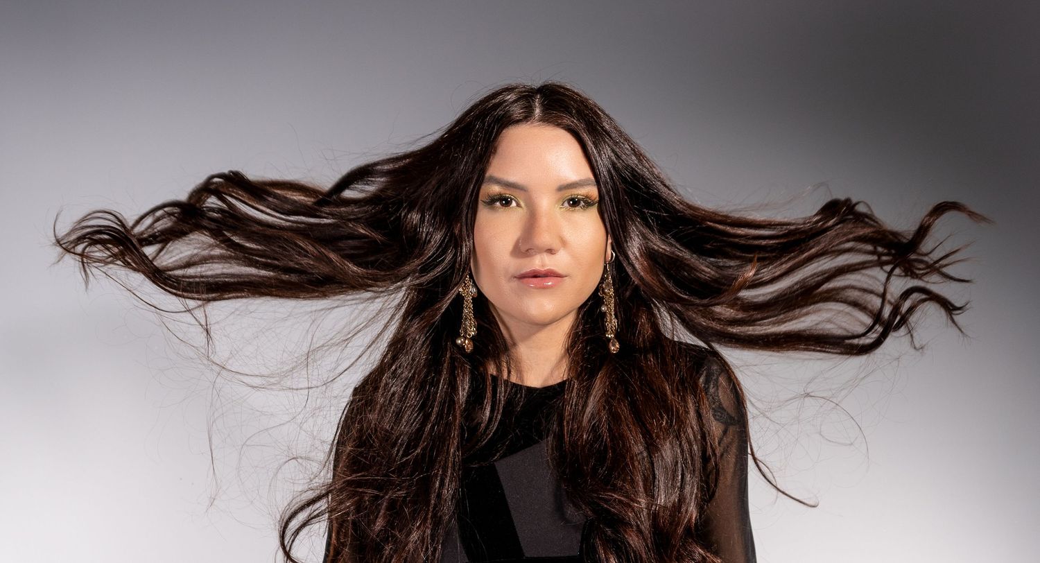 Long dark hair flowing dramatically against a gray studio background with dramatic lighting effect. Artistic portrait photographer.