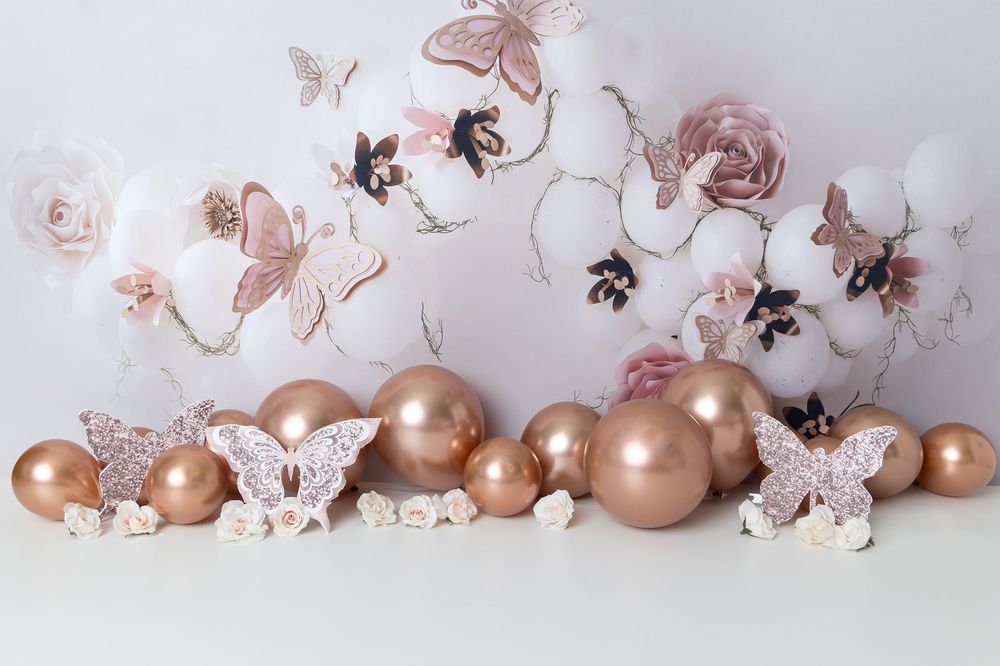 Rose gold Christmas ornaments with delicate butterflies and floral decorations against a white backdrop create an elegant display.