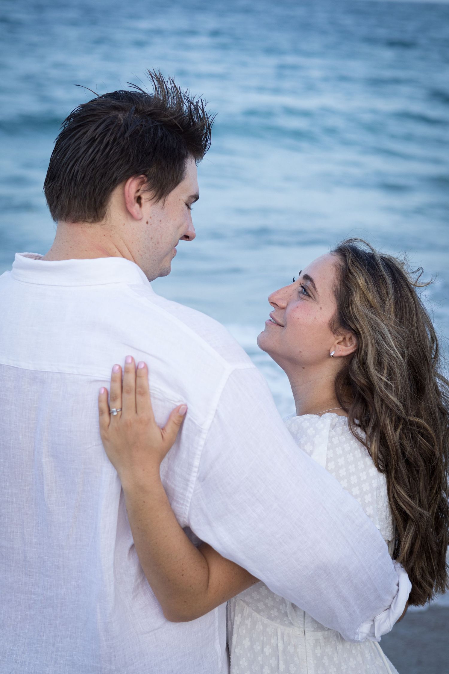 A romantic moment captured between two people by the ocean at dusk.