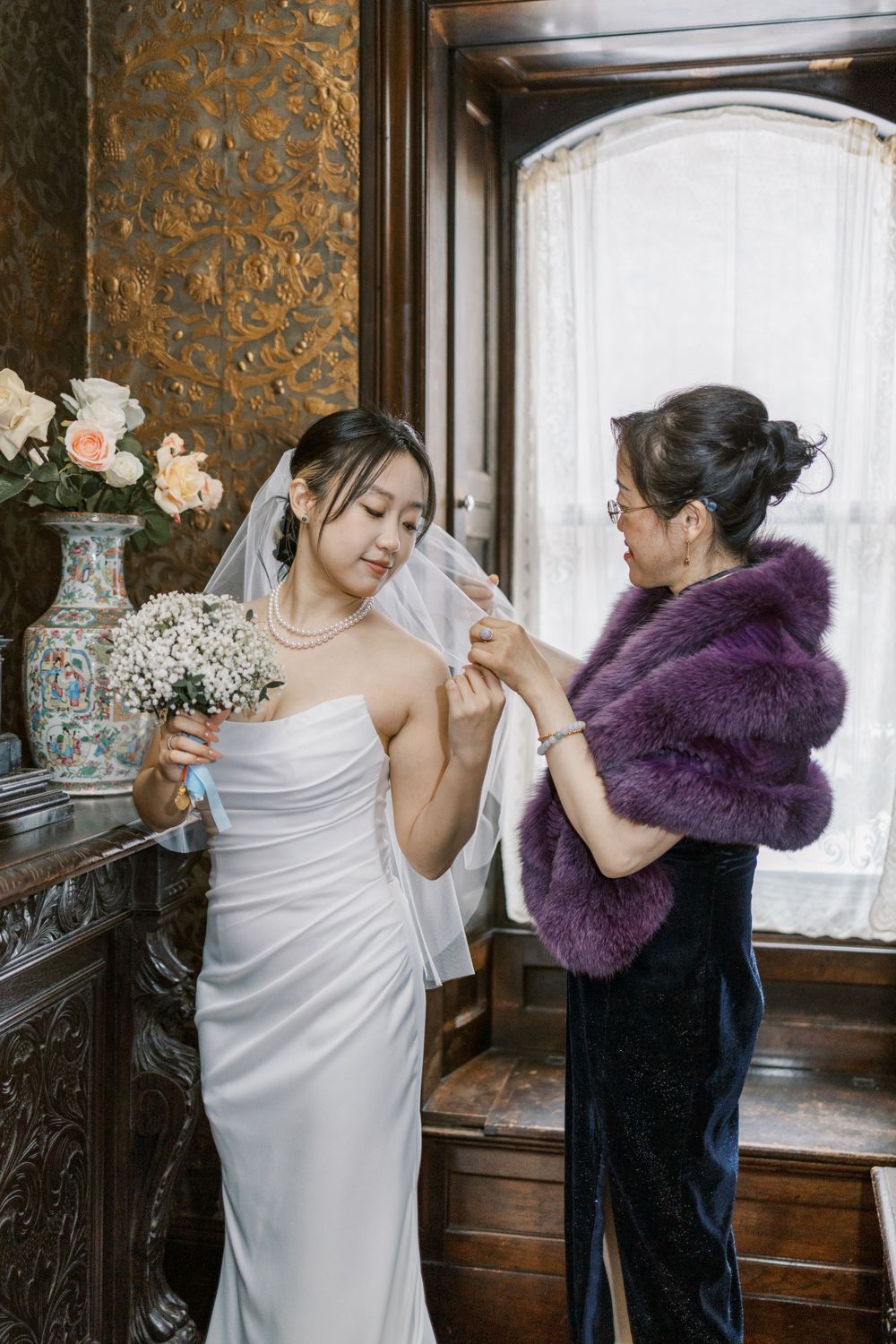 A bride getting final adjustments to her wedding attire in an ornate interior setting.