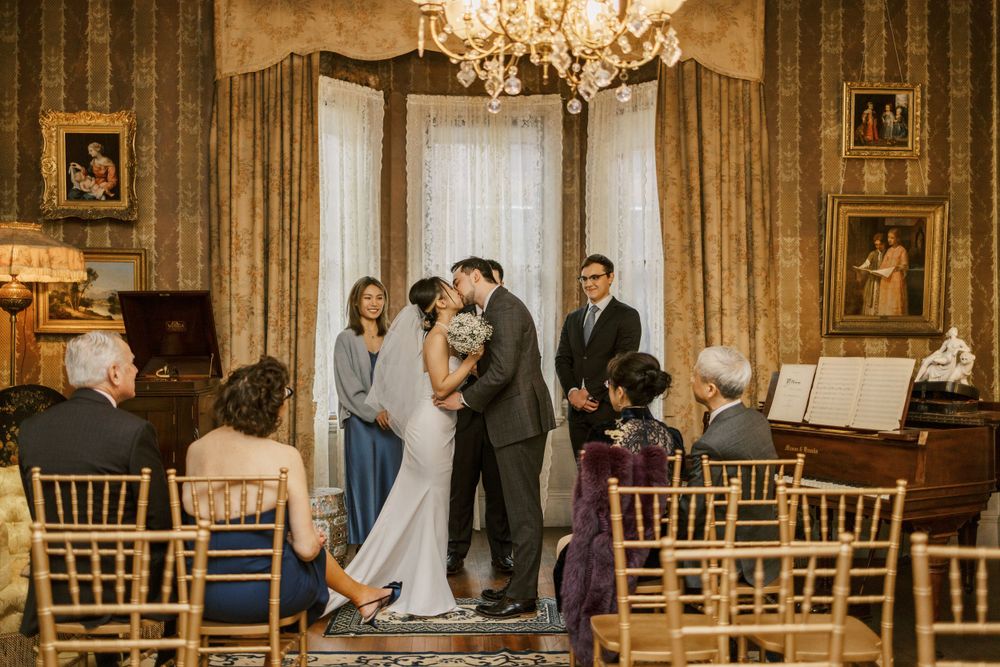An intimate wedding ceremony in a luxurious room with chandelier and gathered guests.