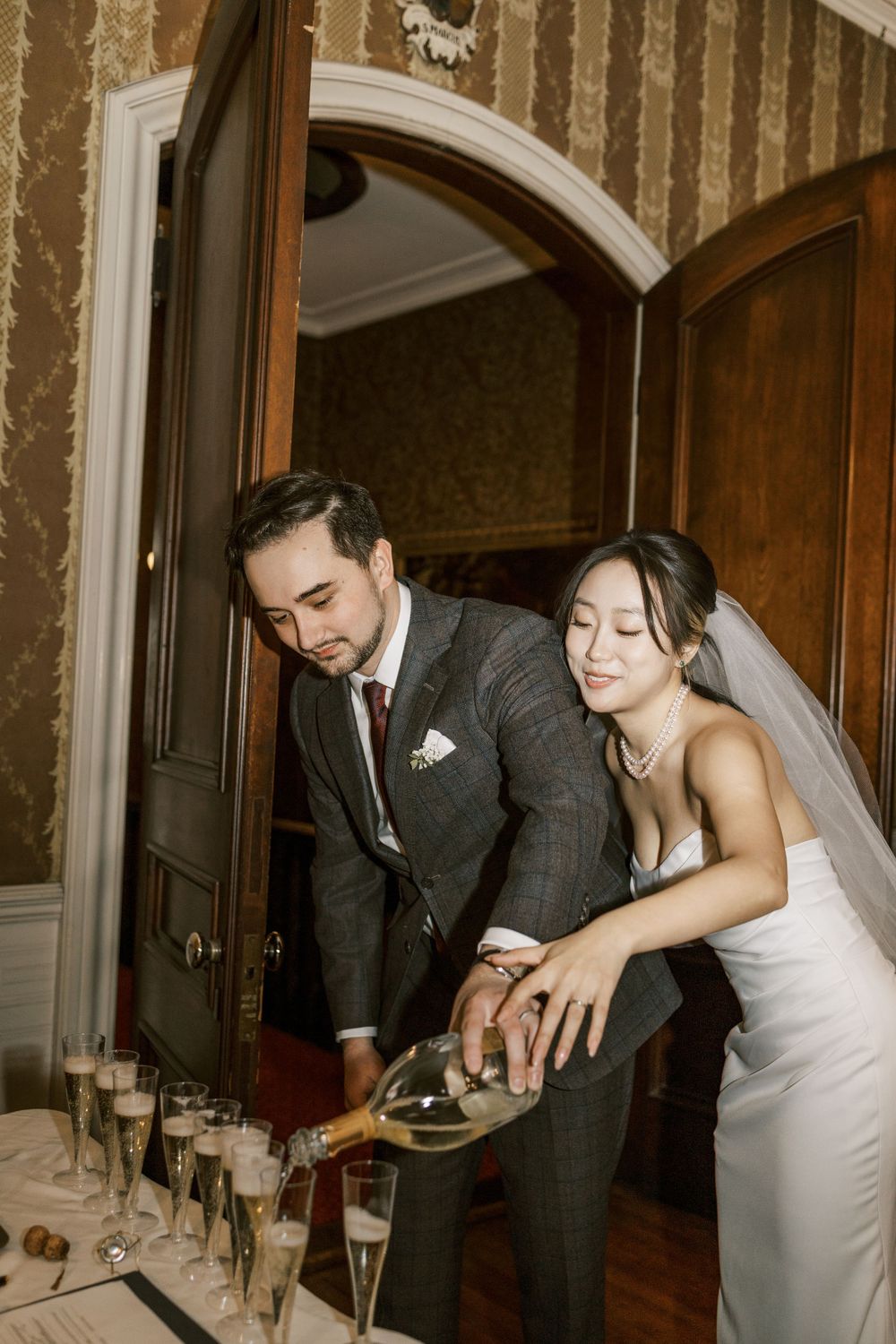 Couple pouring champagne together during their wedding reception in a vintage room.