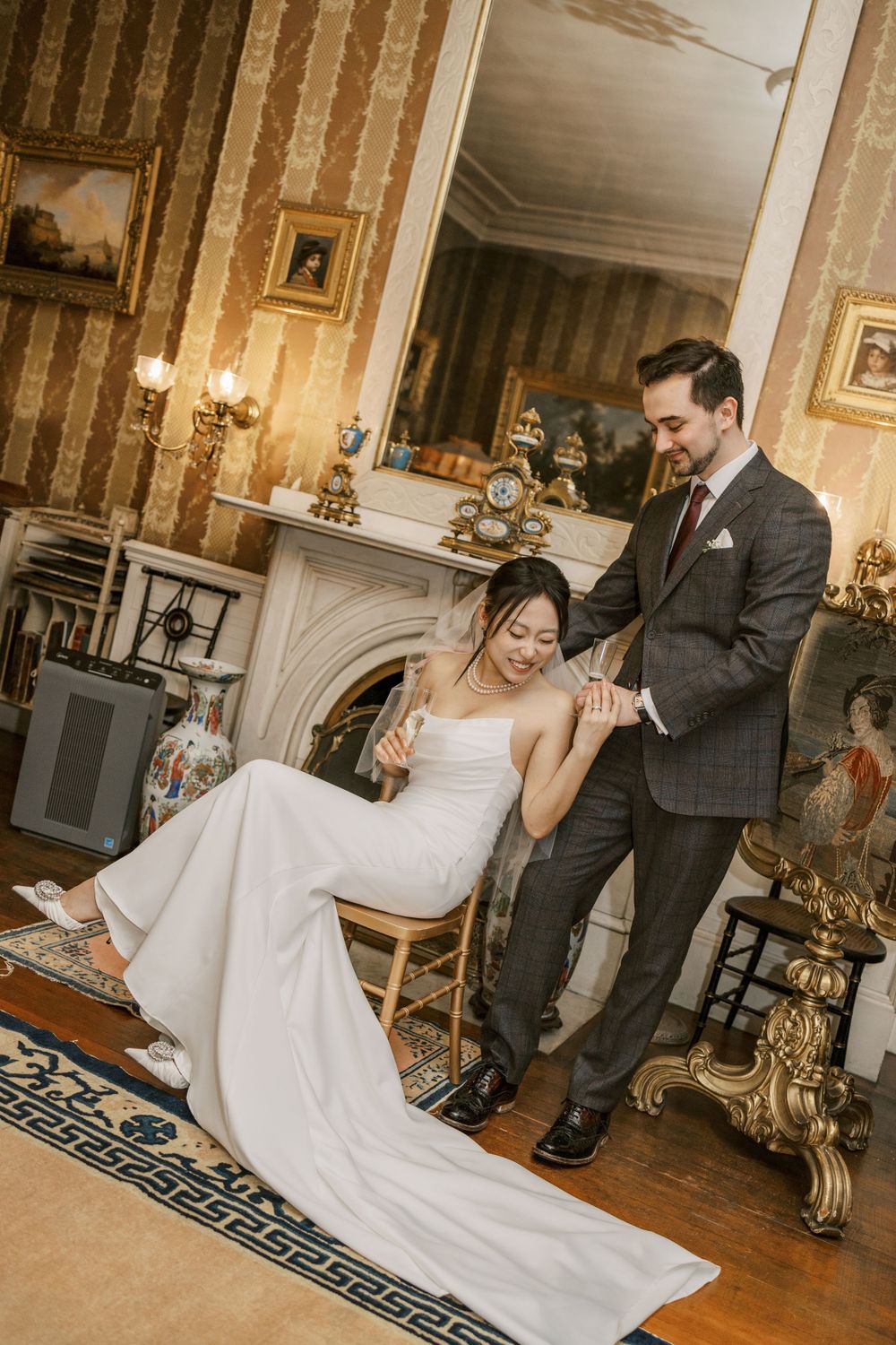 Elegant moment between newlyweds in vintage room with striped wallpaper and fireplace.