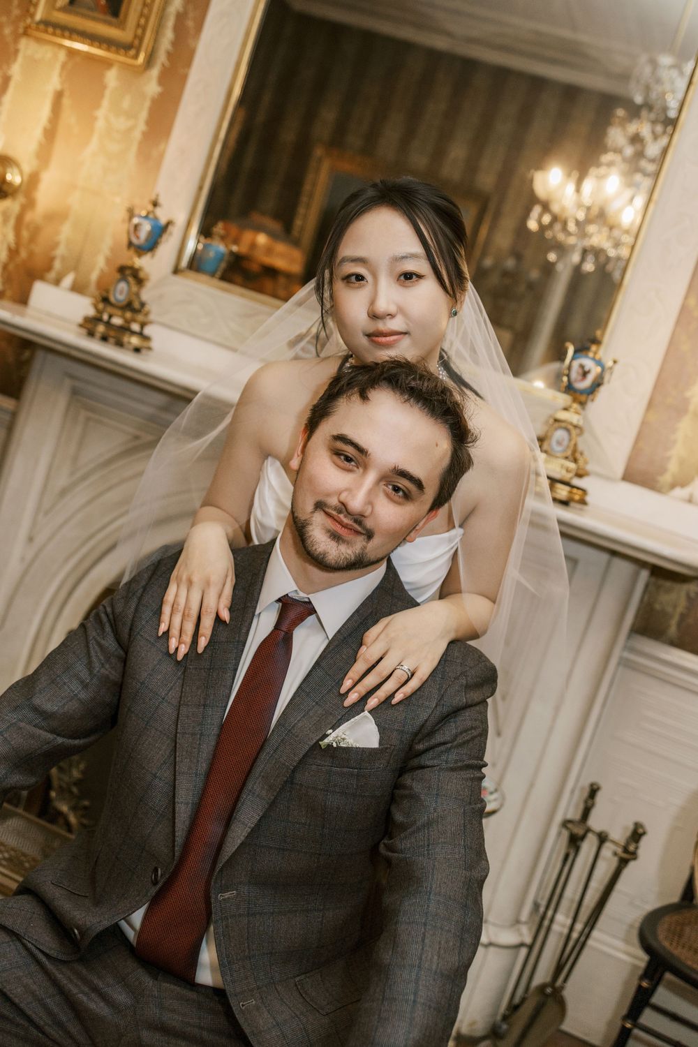 Intimate wedding portrait in front of an ornate fireplace with chandelier.
