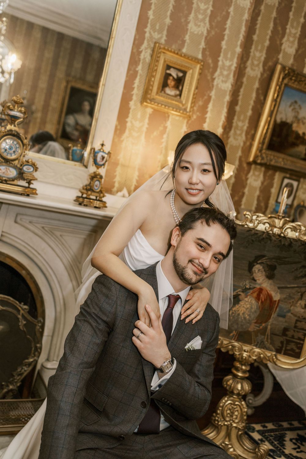 A romantic couple shares a playful moment in an elegant room with ornate decor and vintage furnishings.