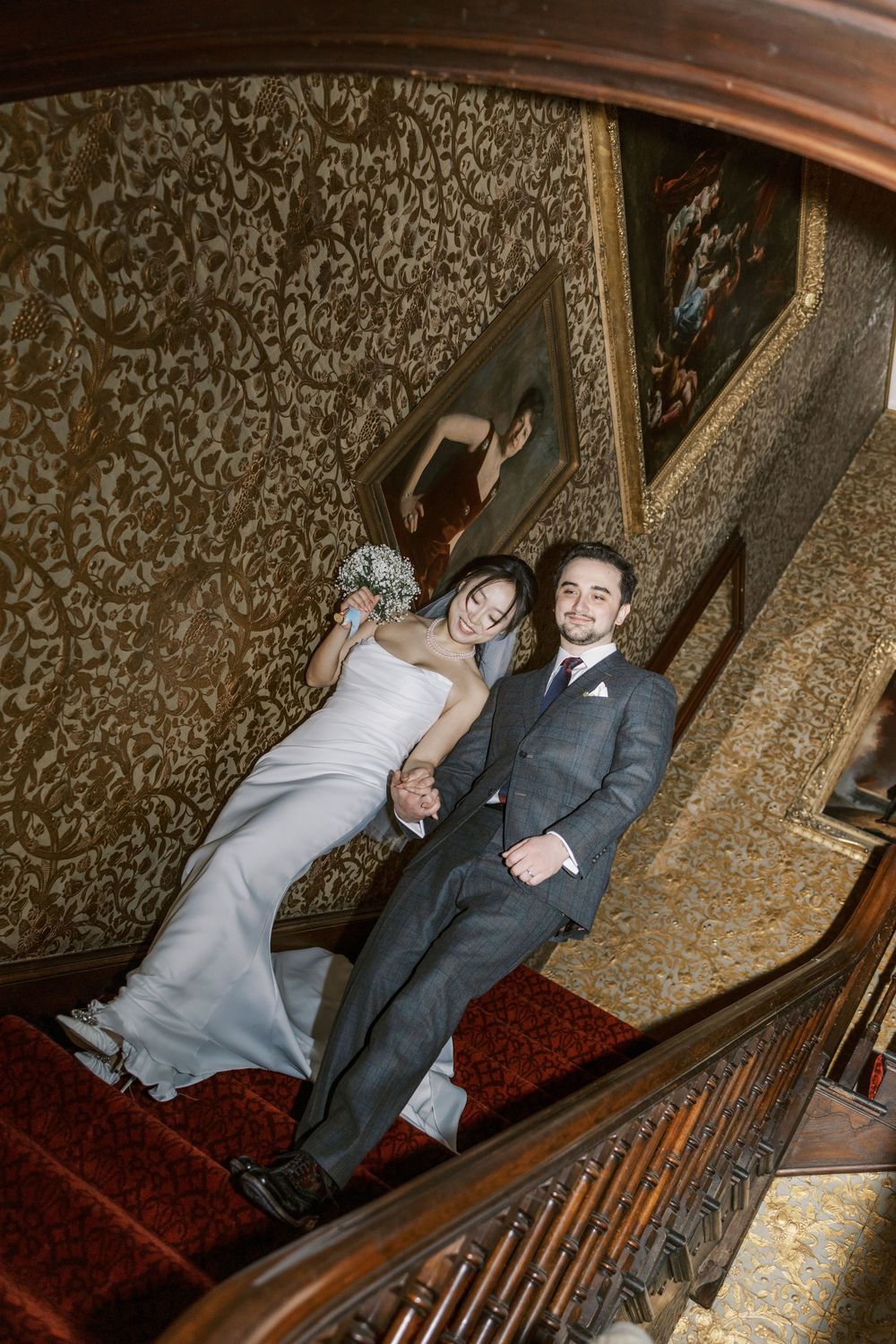 Wedding couple poses on vintage staircase with patterned wallpaper in historic venue.