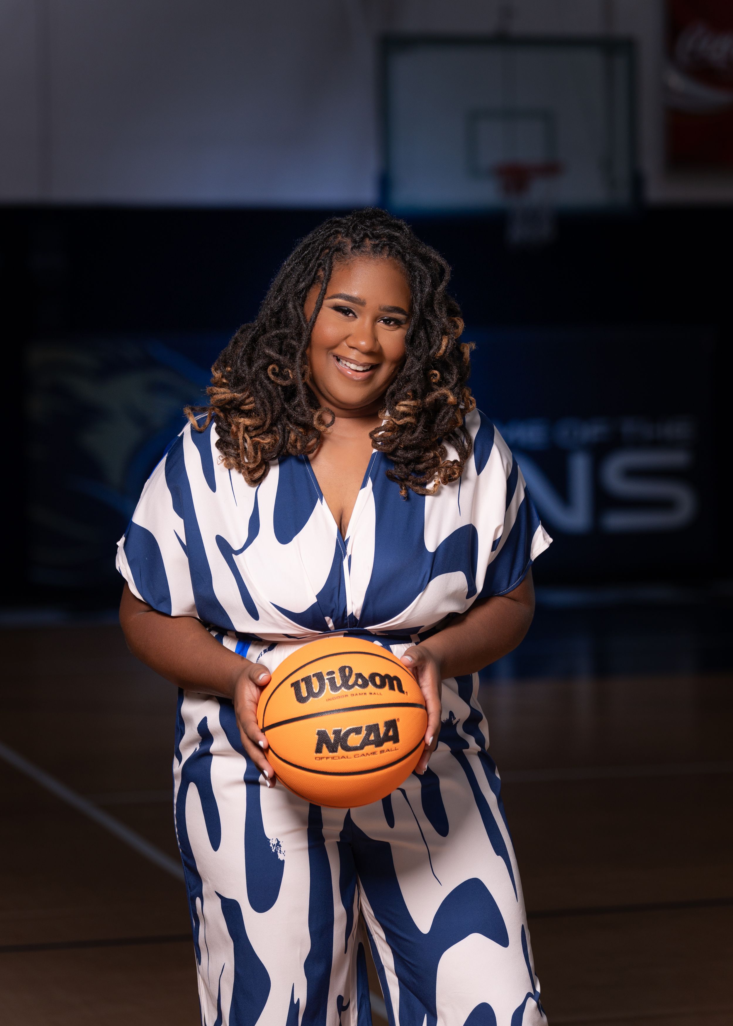 Basketball player in blue and white patterned outfit holds Wilson NCAA basketball on indoor court.