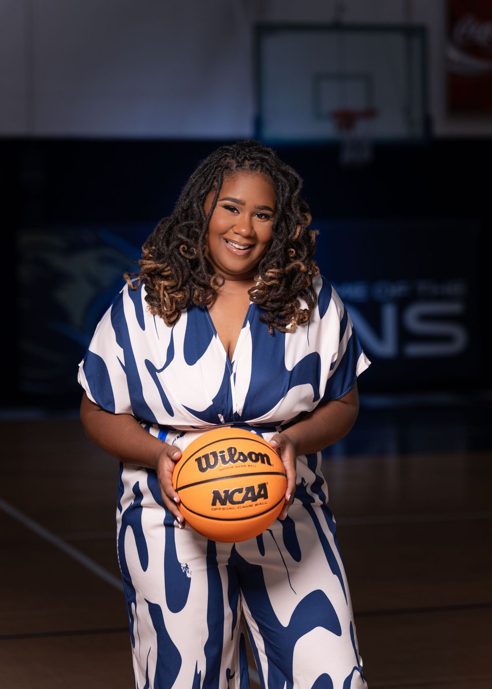 Basketball player in blue and white patterned outfit holds Wilson NCAA basketball on indoor court.