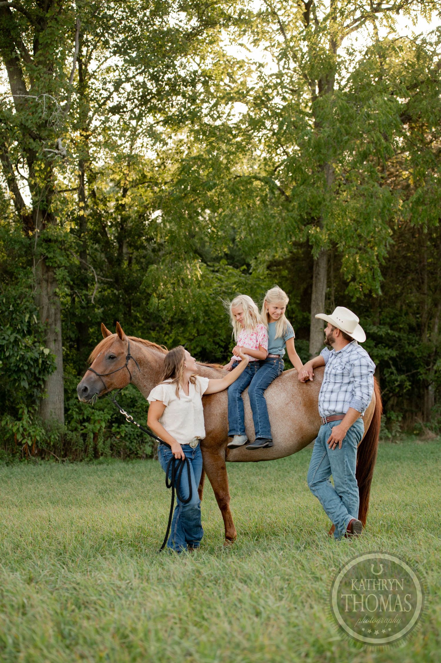 A family gathers around their horse in a peaceful countryside setting during golden hour.