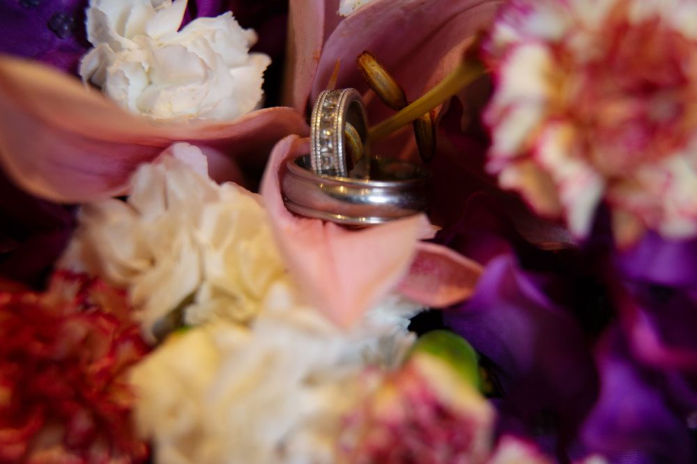 Wedding rings nestled among colorful carnations and roses in pink, purple, and white hues.