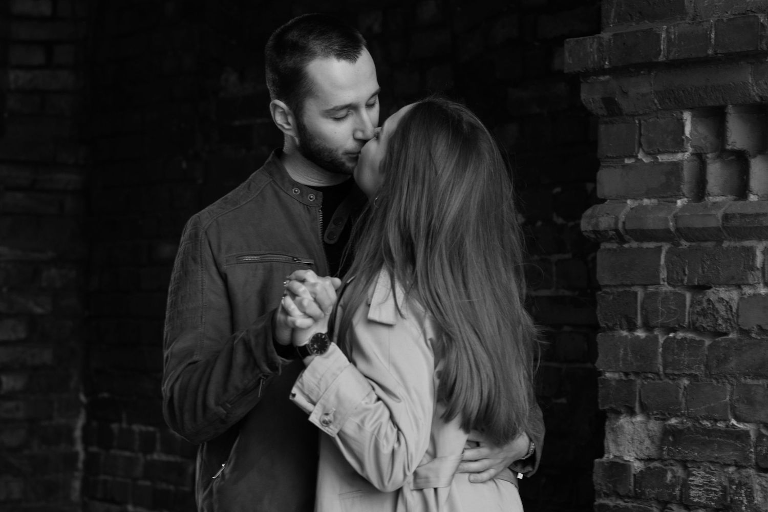 A romantic black and white moment of a couple dancing together against a rustic brick wall.