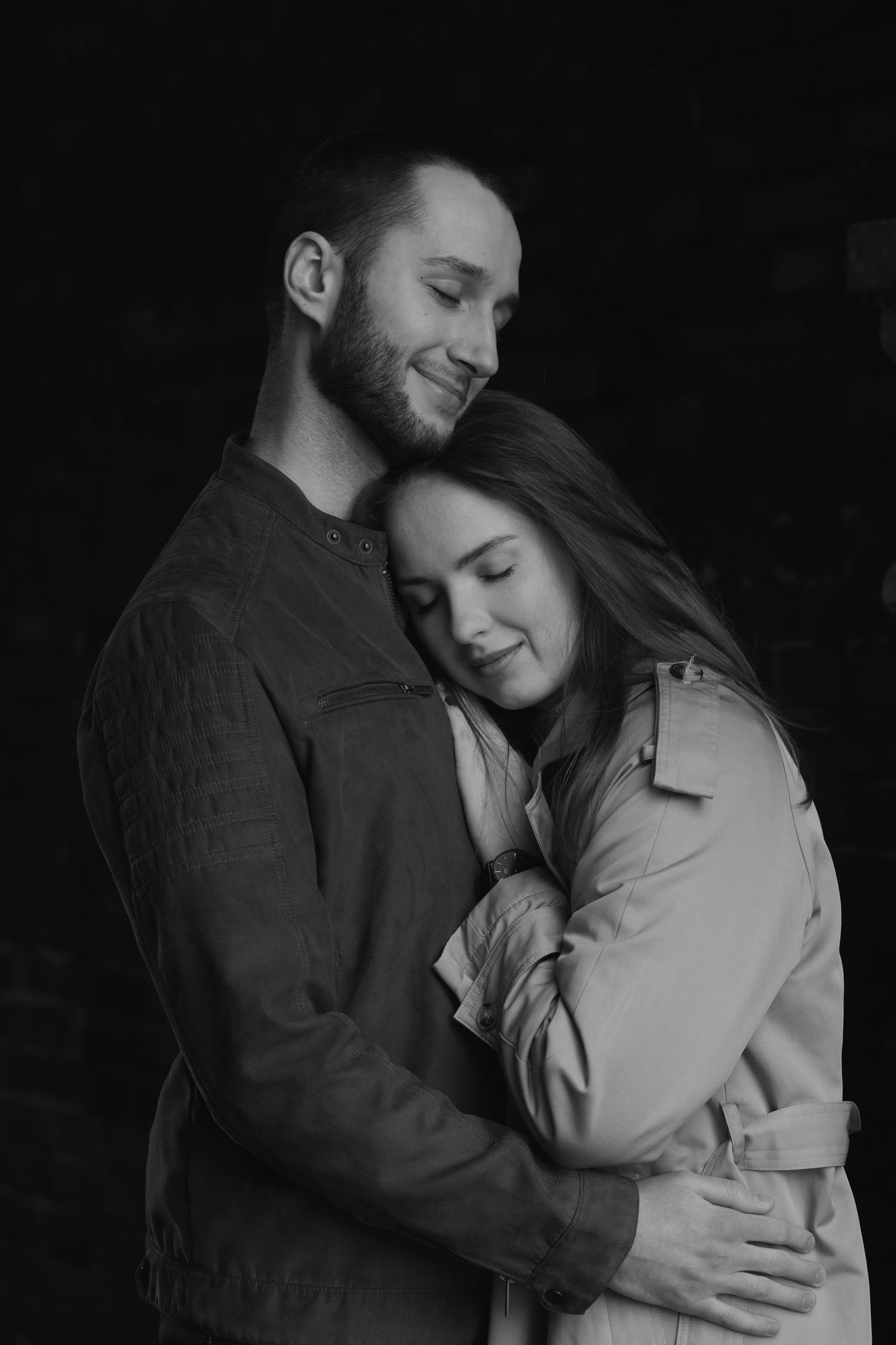 A romantic black and white portrait of a couple embracing tenderly against a dark background.