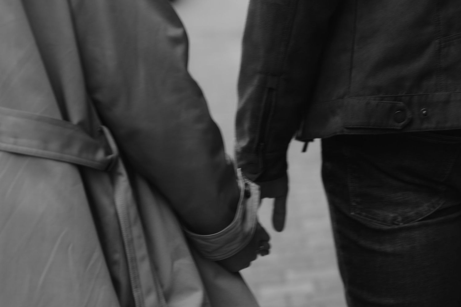 Black and white close up photograph of two people holding hands while wearing jackets and jeans.