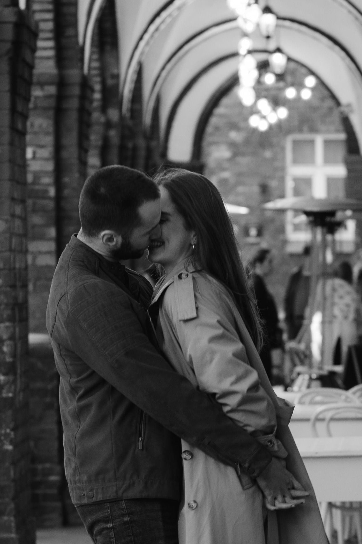 A romantic black and white shot of a couple sharing an intimate moment under an arched passageway.