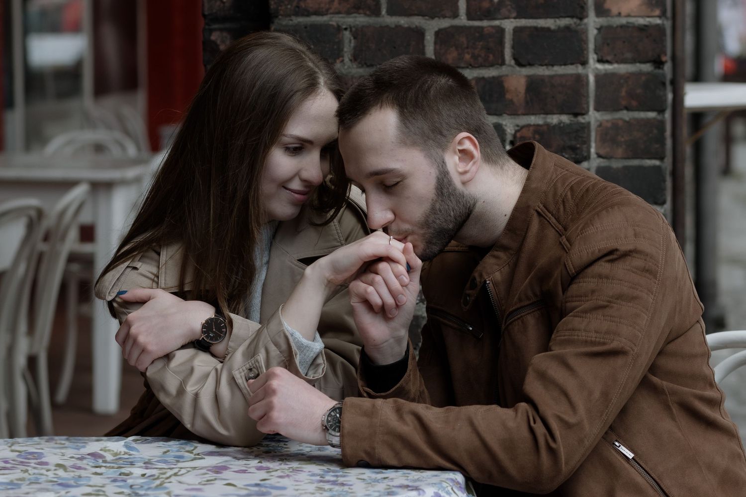 A tender moment shared between a couple leaning close together at an outdoor table.