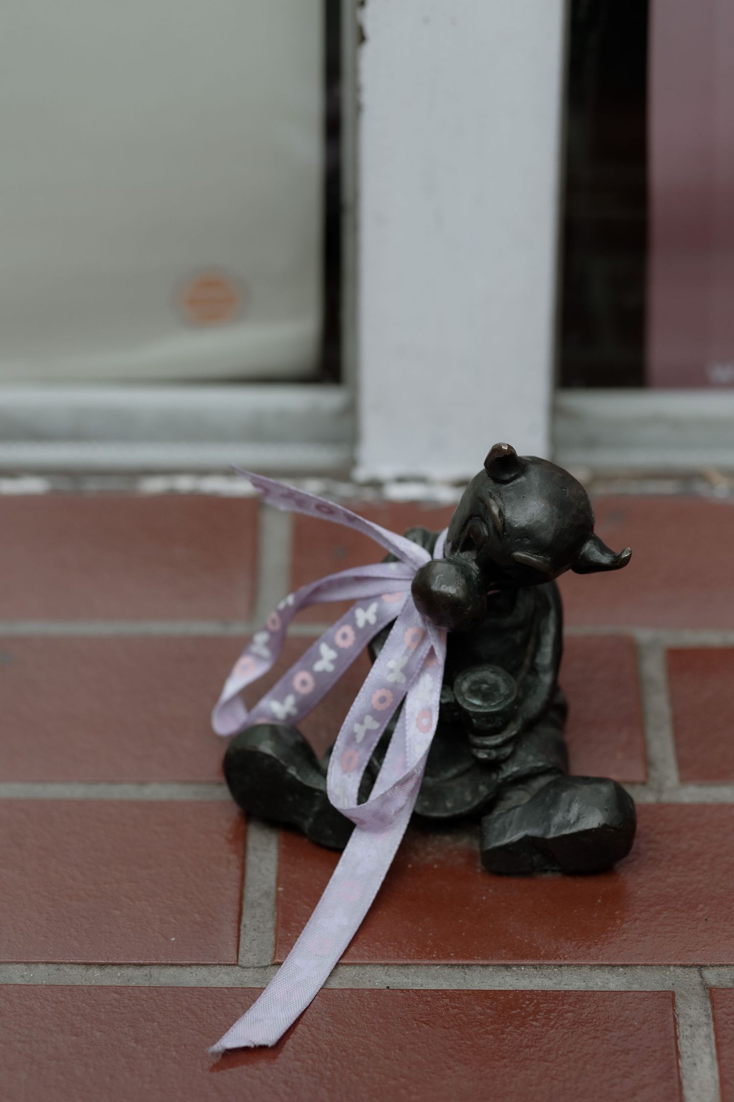 A small black decorative pig figurine with a pink ribbon sitting on terracotta tiles.