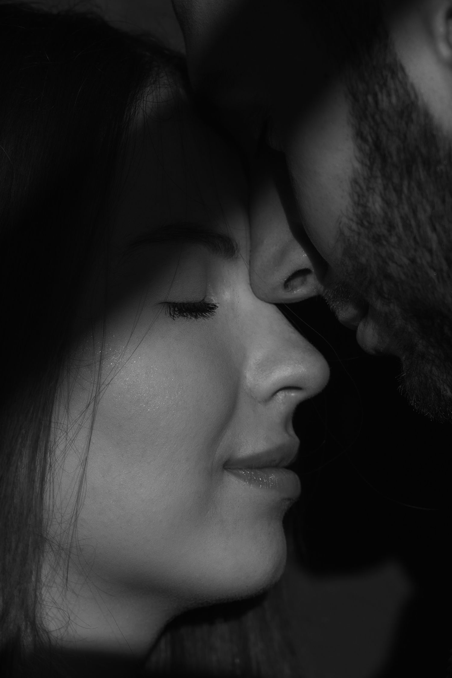 Close-up black and white intimate portrait showing two lovers in a tender moment with eyes closed as they lean in close.