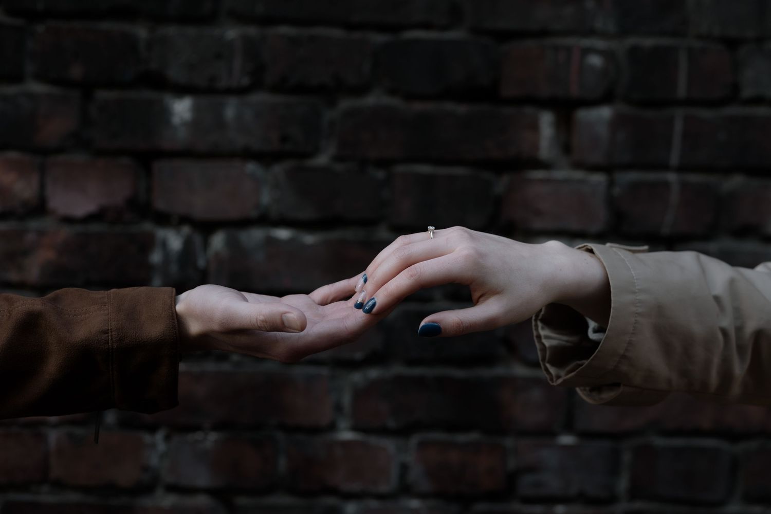 Two hands reaching out and touching against a dark brick wall background in a moody atmospheric setting.