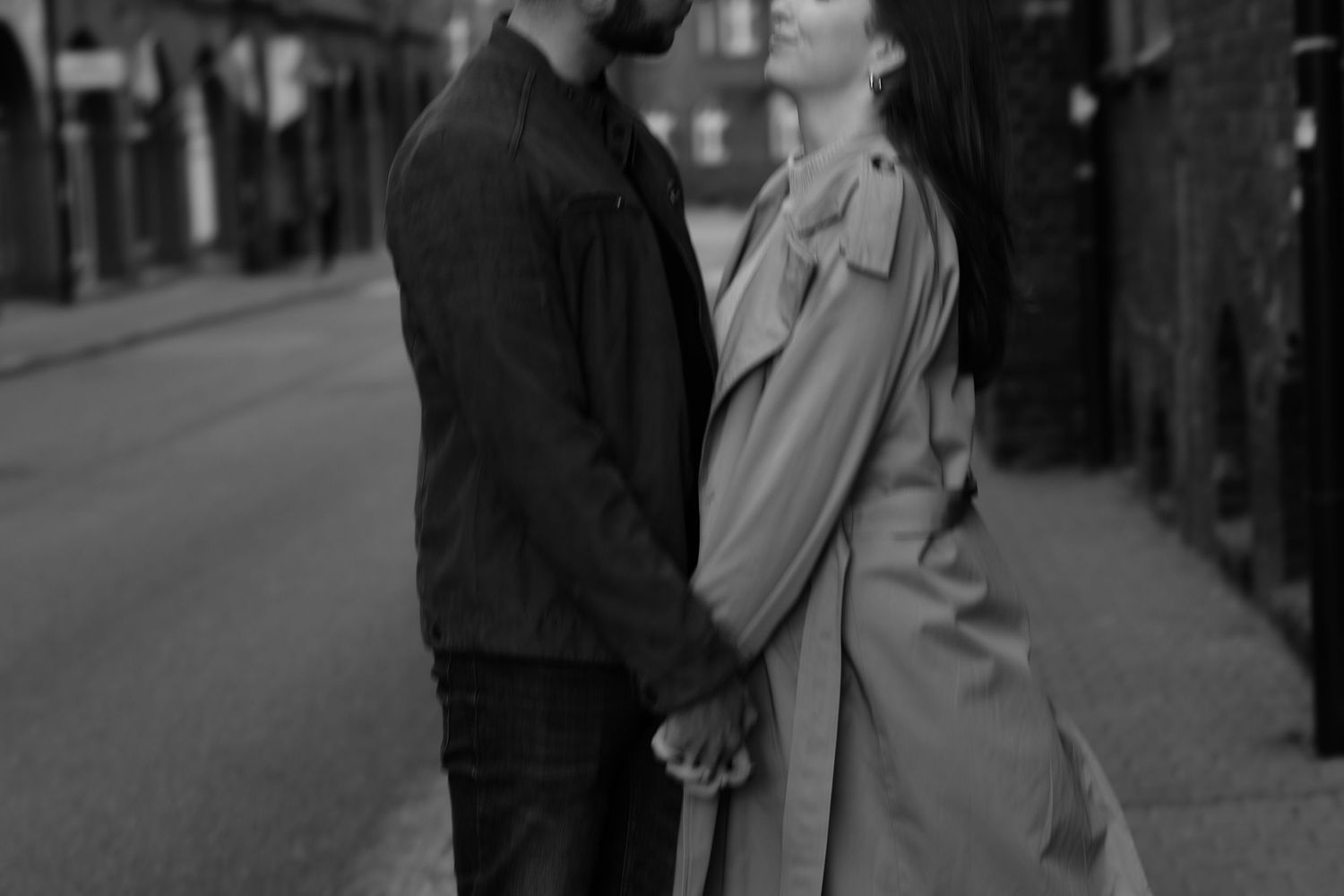 A romantic black and white street scene of a couple holding hands while standing close together on a sidewalk.
