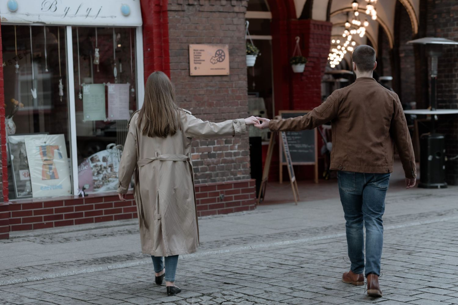 Two people walking together on a snowy street while pointing at storefronts in a winter scene.