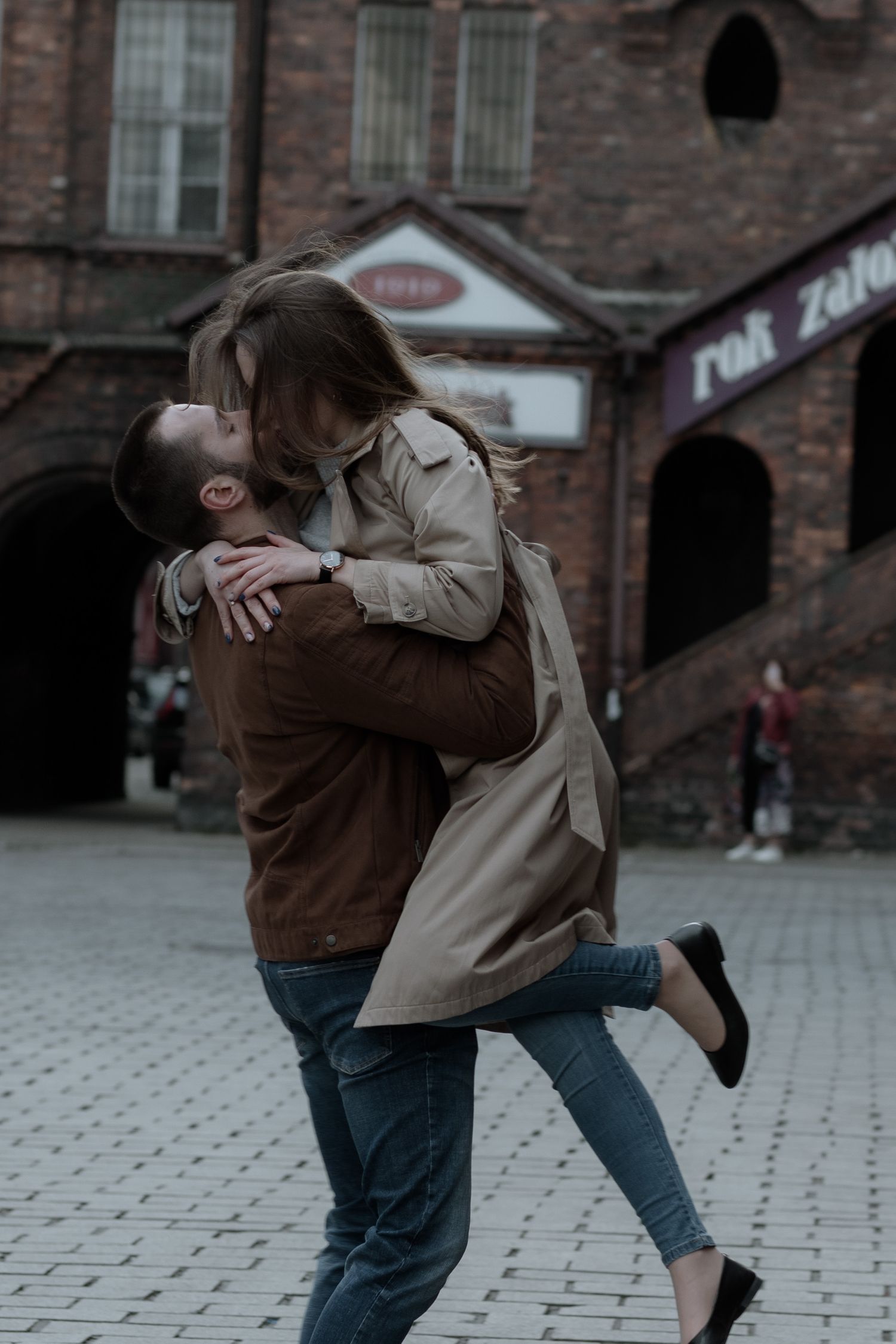 A romantic moment captured on cobblestone street with historic brick building in background on moody overcast day.