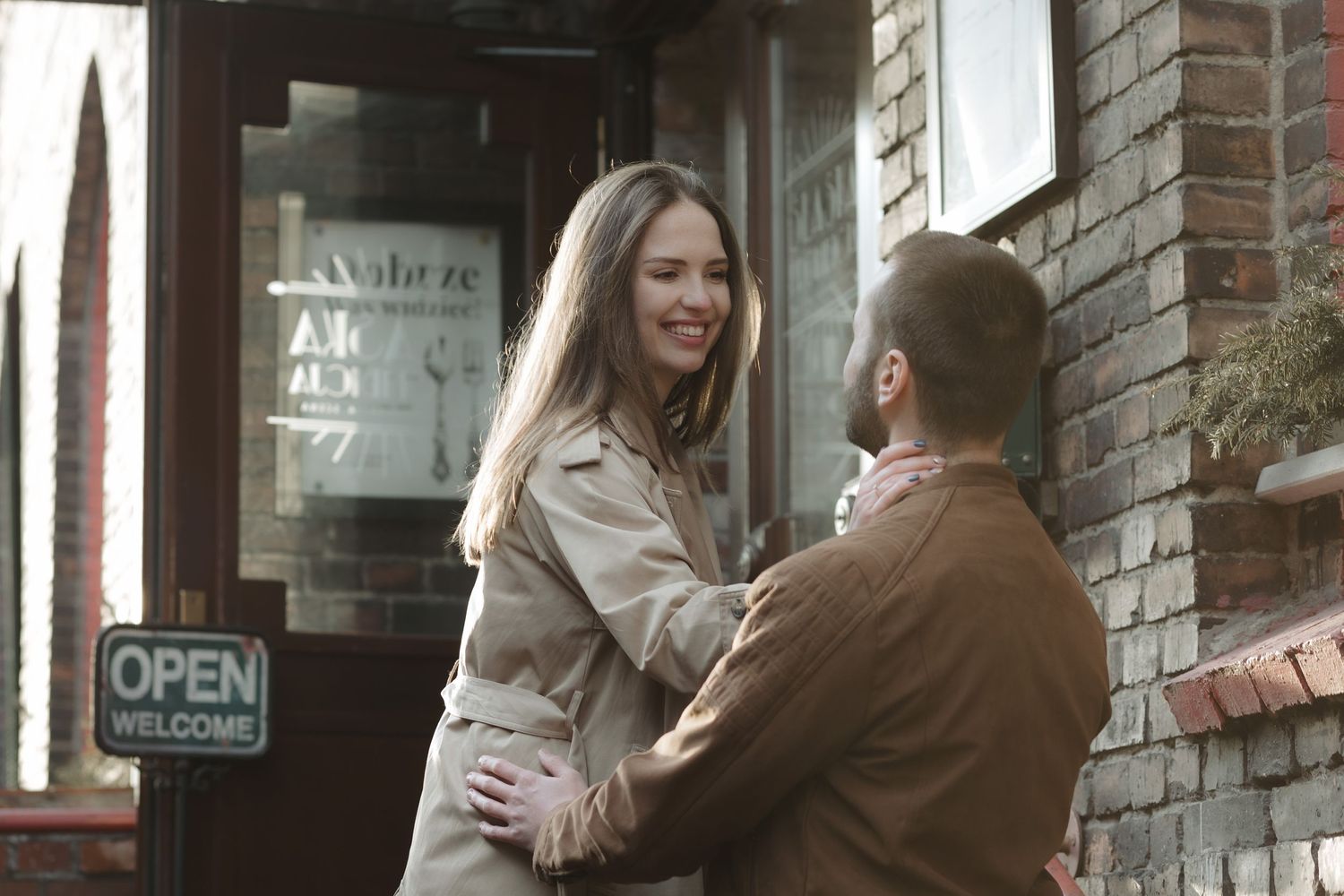 Two people share a romantic moment outside a brick building with an open sign in view.
