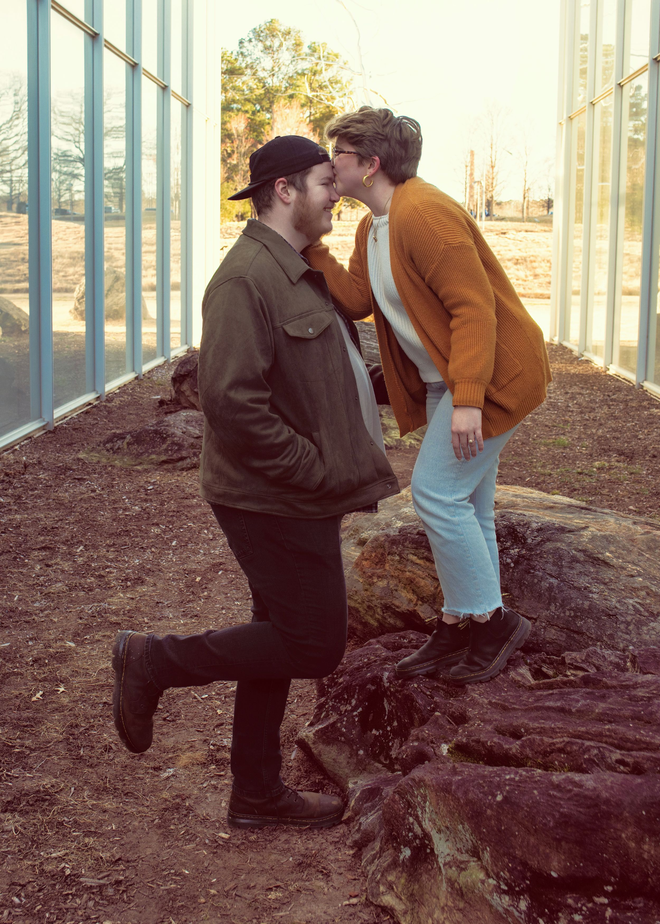 A romantic sunset scene with two people sharing an intimate moment on rocky terrain in warm autumn lighting.