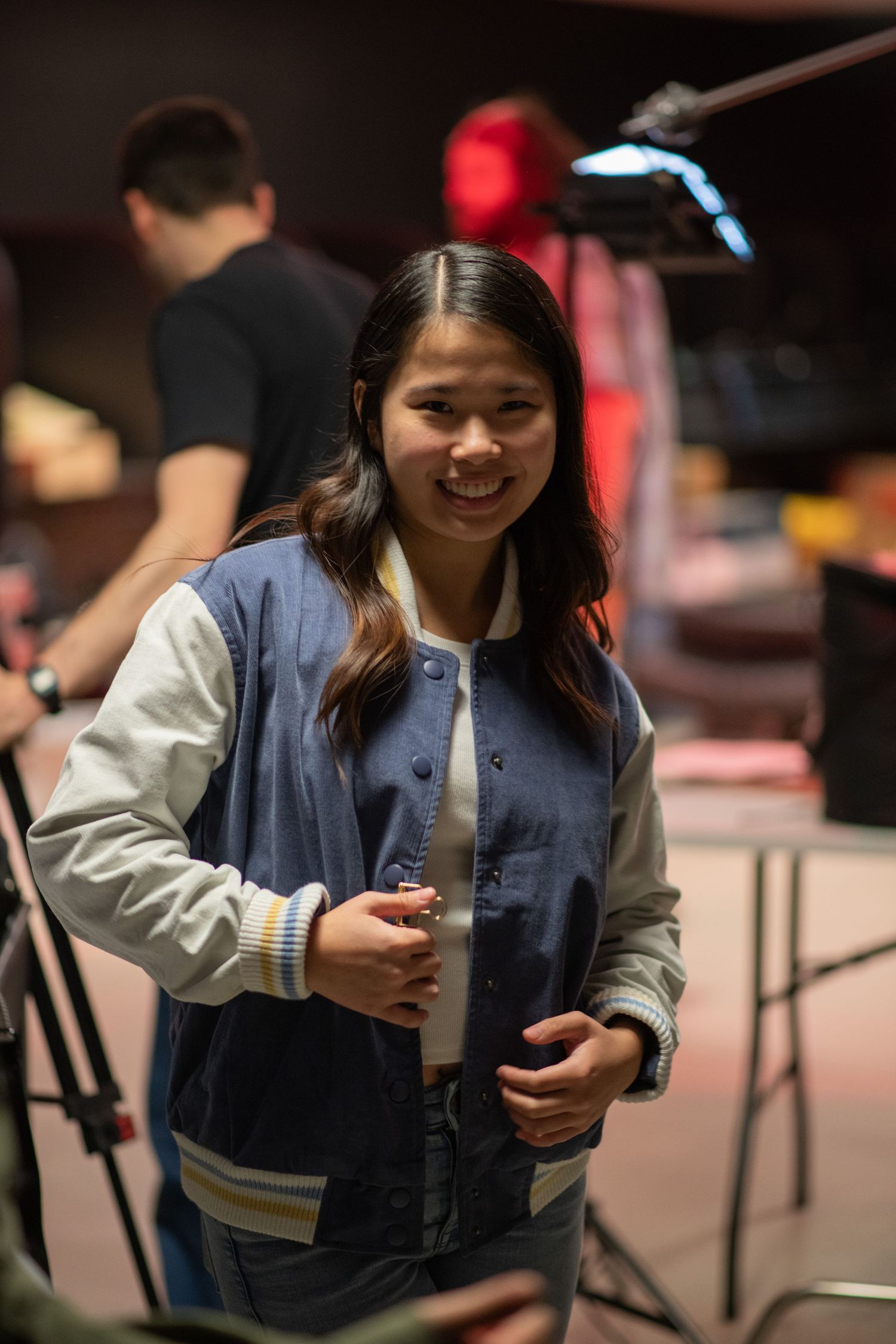 Smiling young woman in blue varsity jacket on a film production set.