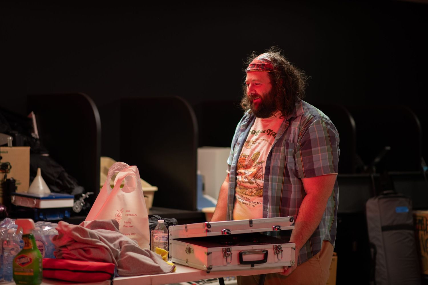Bearded man in plaid shirt standing near props on a red-lit film set.