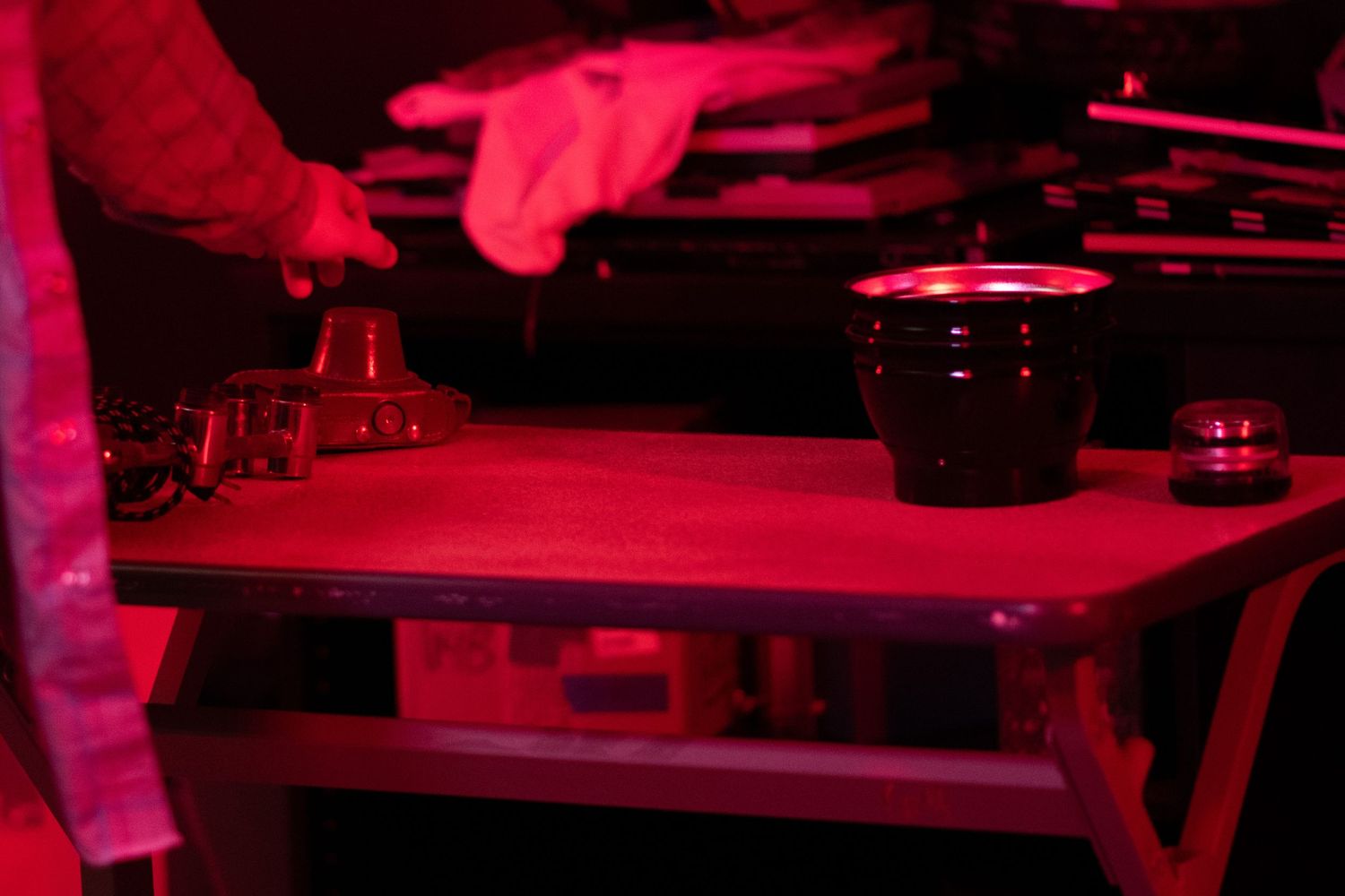 Close-up of a wooden table with camera lenses and a black bowl under red lighting on a film set.