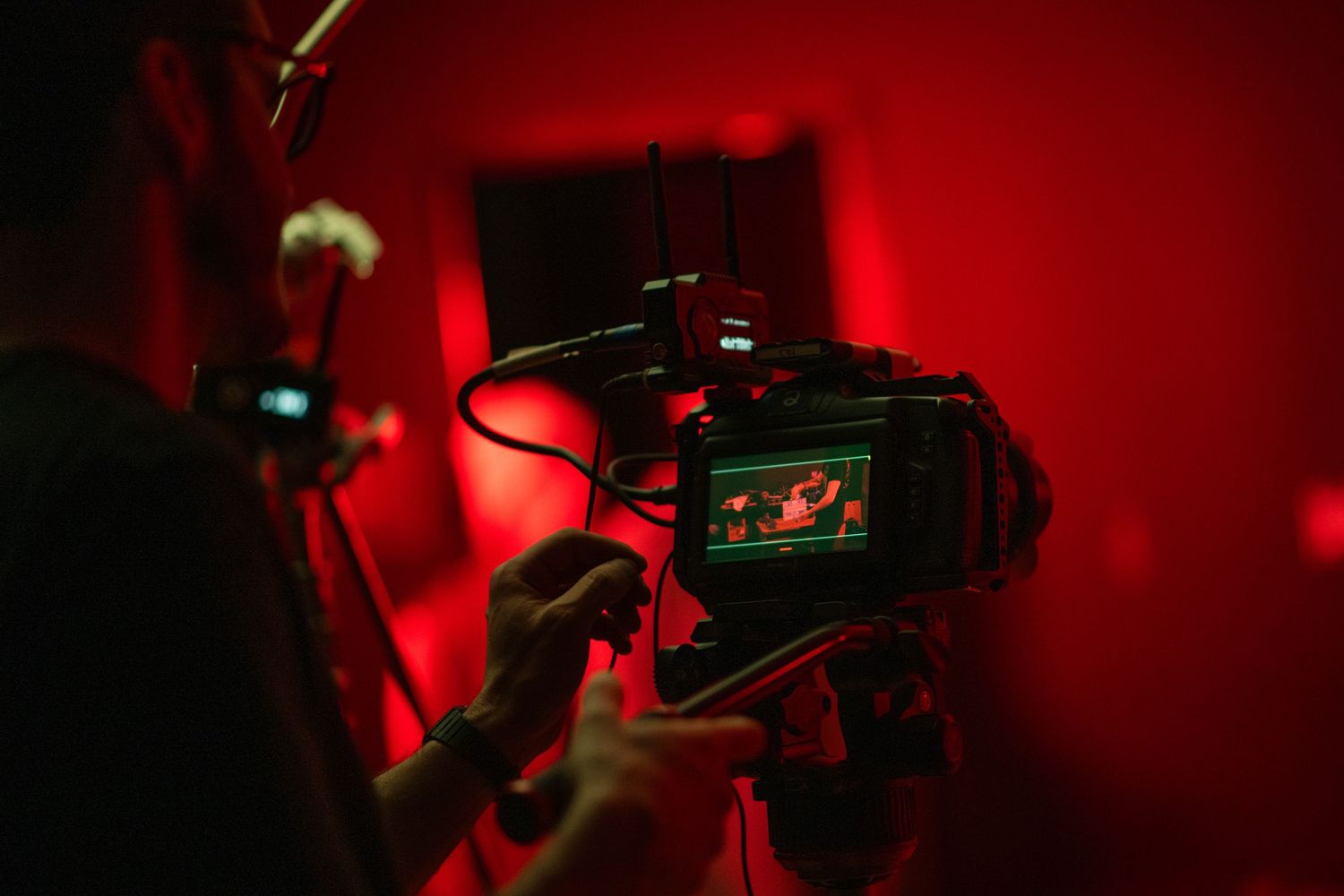 Cameraman filming with a DSLR camera on a red-lit film set with monitor displaying live footage.