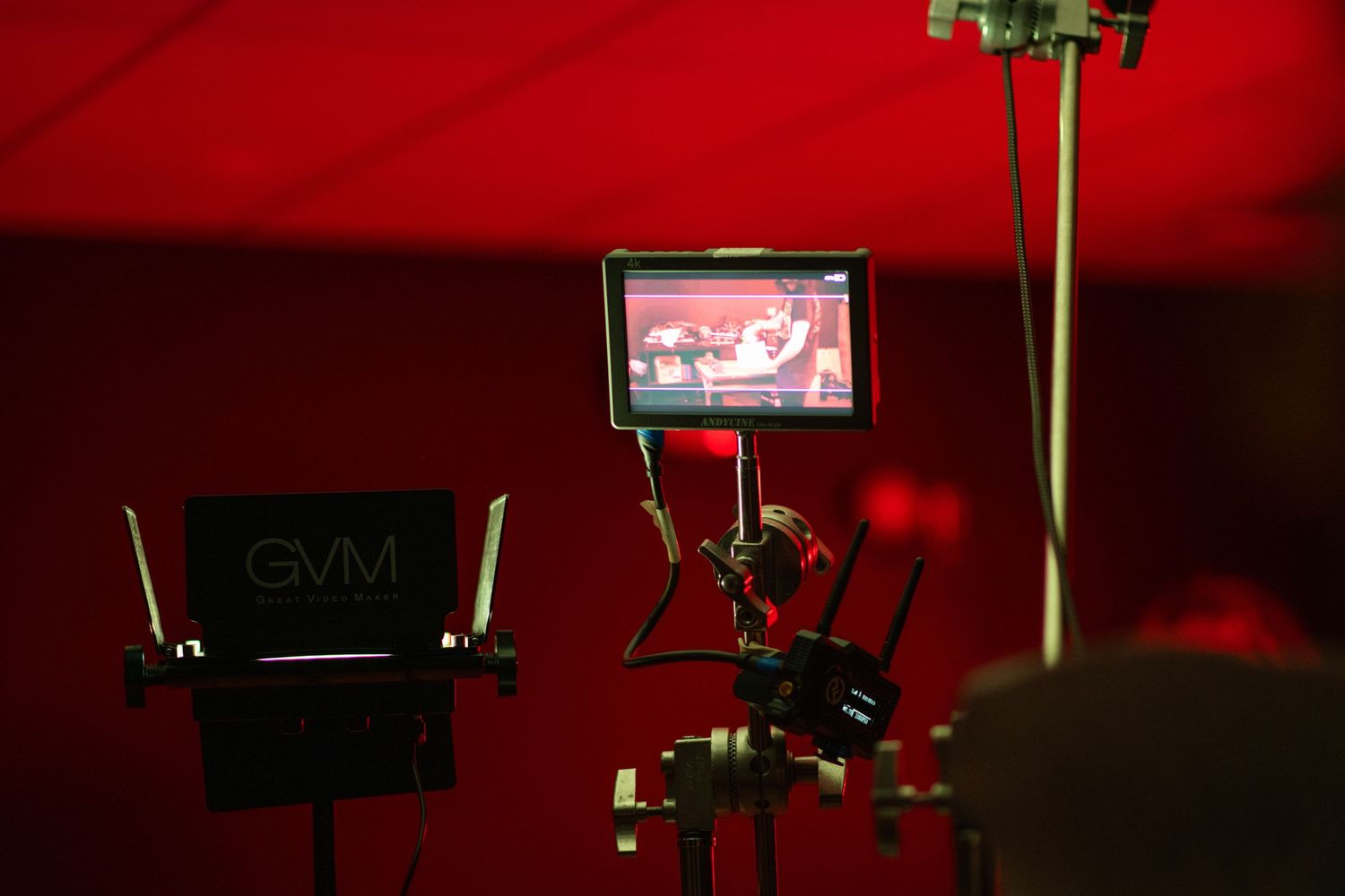 GVM monitor and camera equipment on a film set with a red background displaying footage on screen.