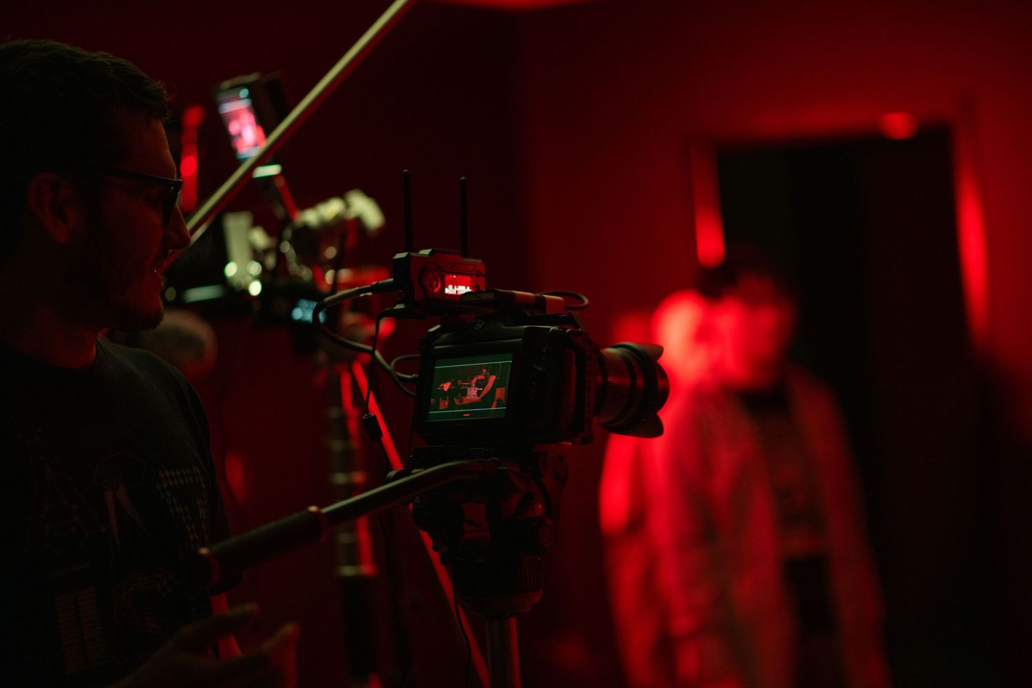 Camera operator filming with professional equipment on a dramatic red-lit film set.
