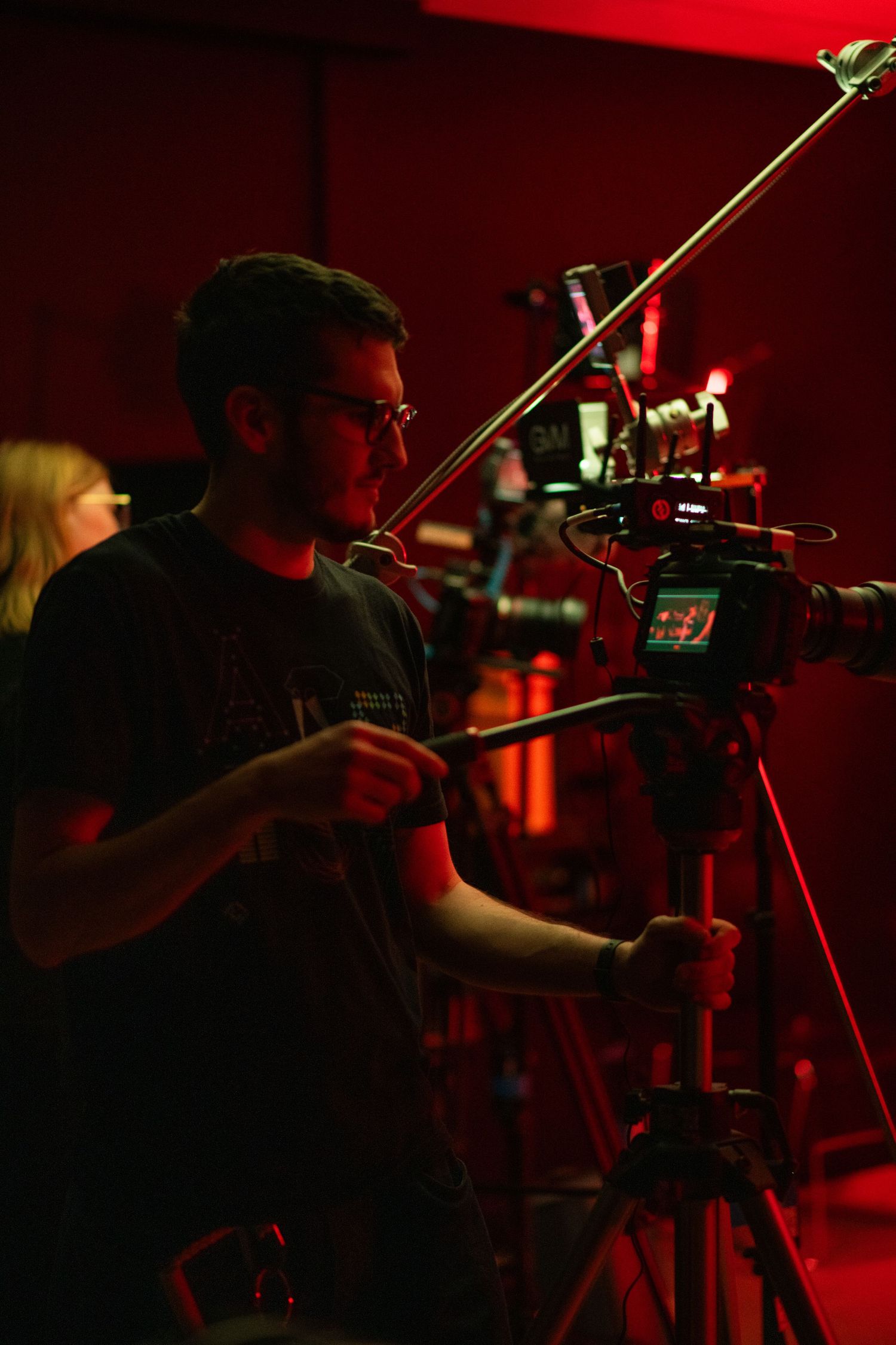 Male cinematographer adjusting a professional camera on a red-lit film production set.
