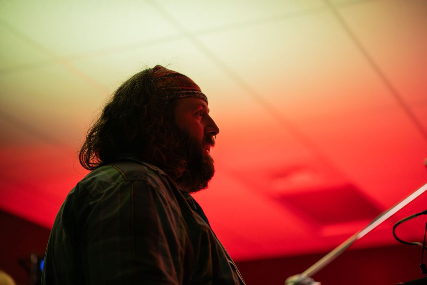 Side profile of a bearded man with long hair illuminated by red and yellow lighting on a film set.